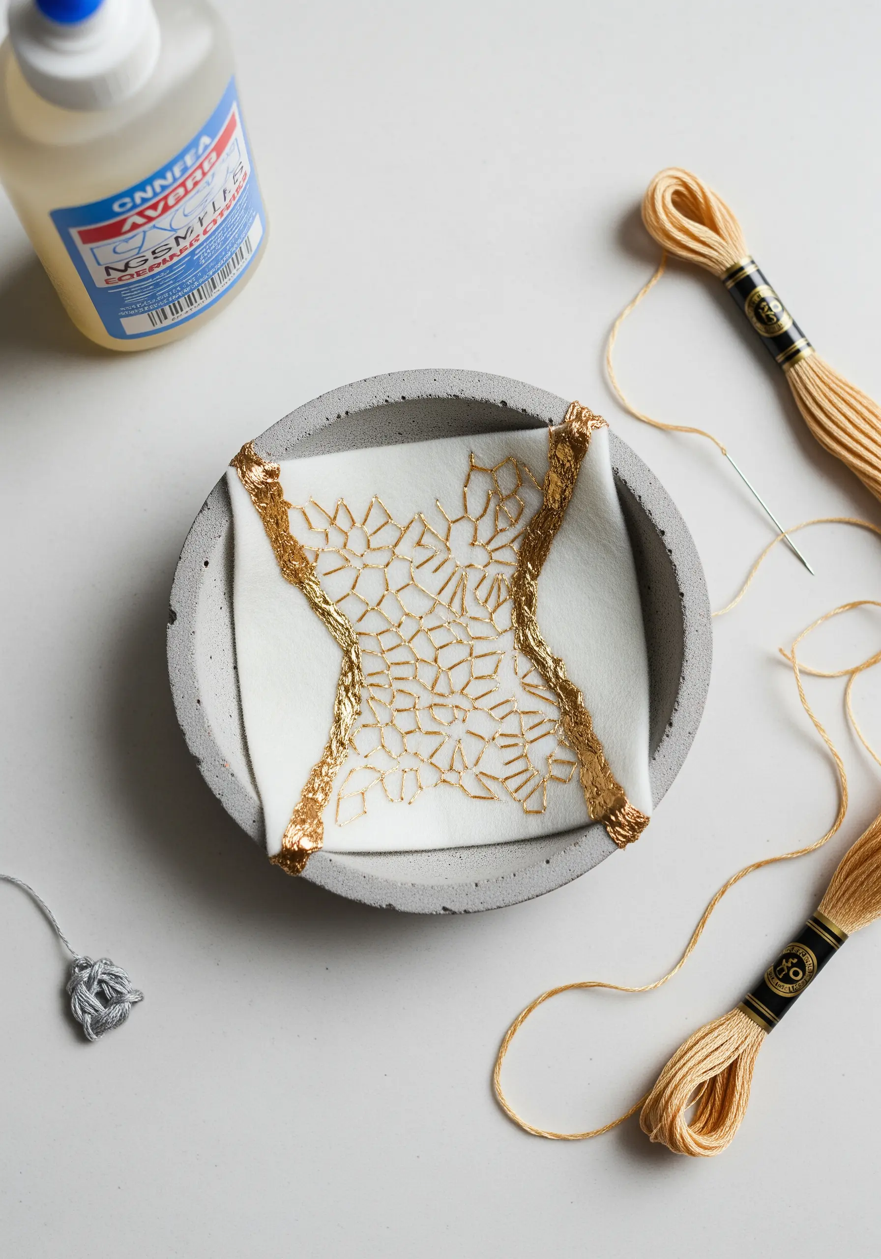 An embroidered piece with a goldwork web pattern, edged in gold leaf, set in a concrete dish.
