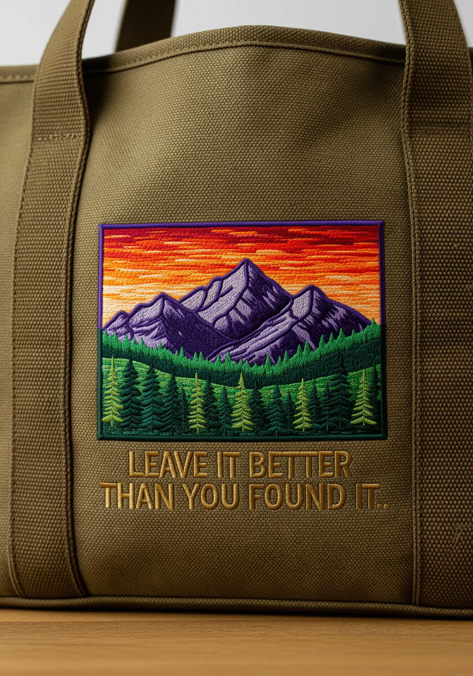 An embroidered patch of a mountain scene at sunset on an olive green tote bag.