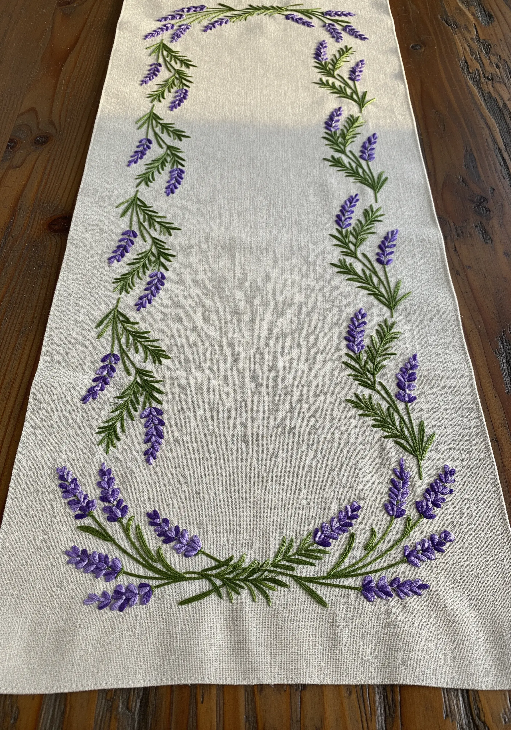 Embroidered lavender sprigs forming a rectangular border on a cream table runner.