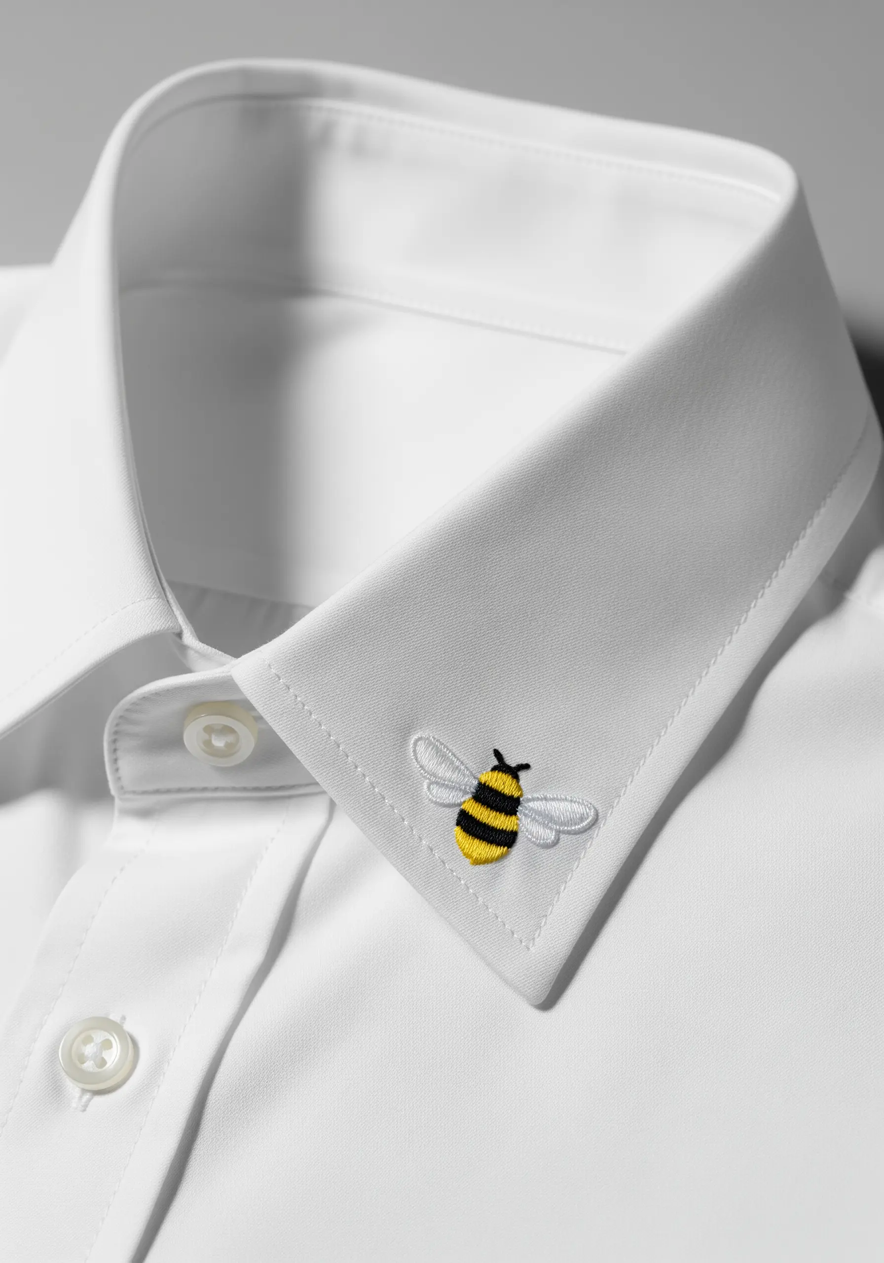 A tiny, detailed embroidered bee with translucent wings on a white shirt collar.