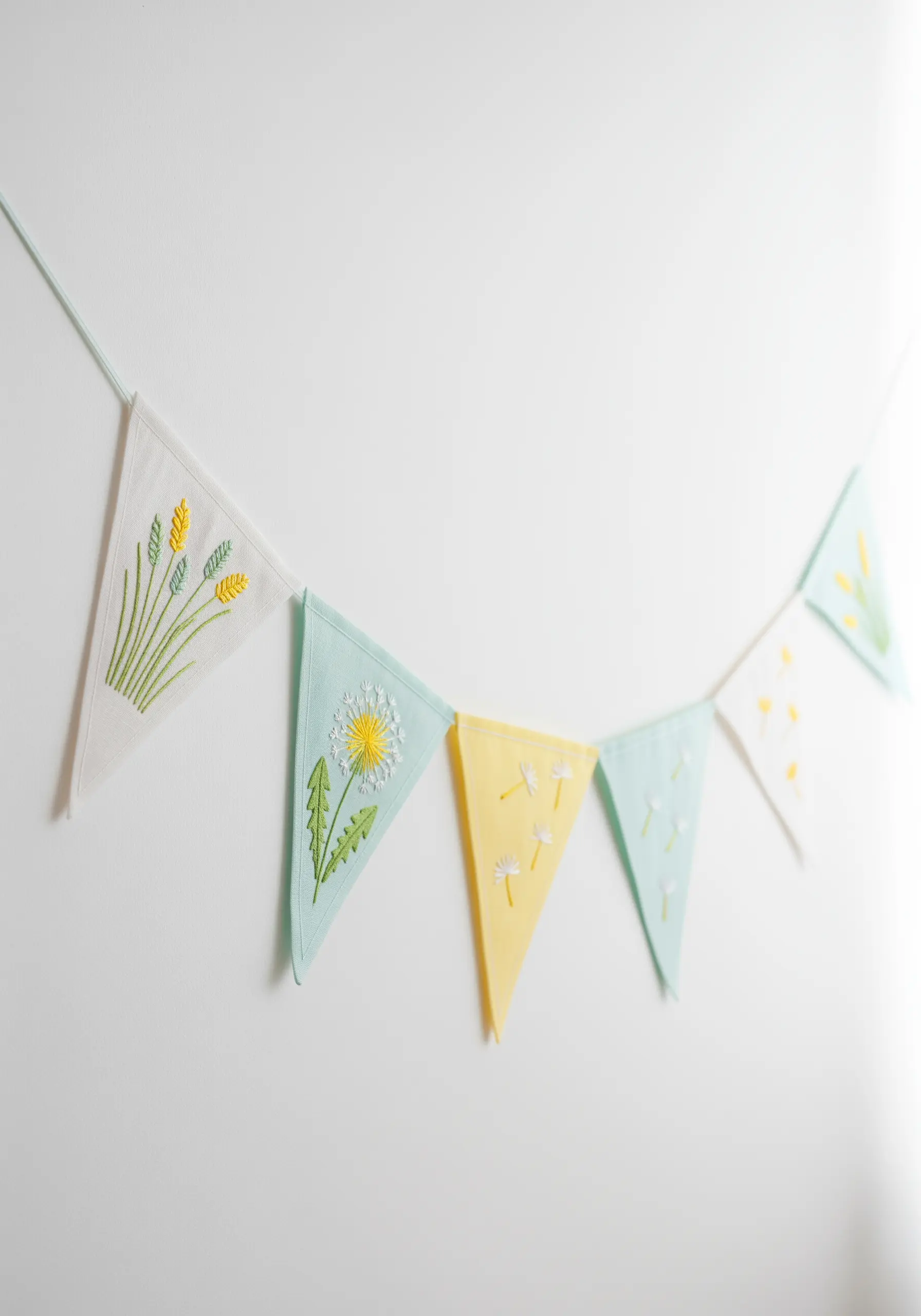 A multi-colored bunting with different dandelion and wildgrass motifs on each flag.