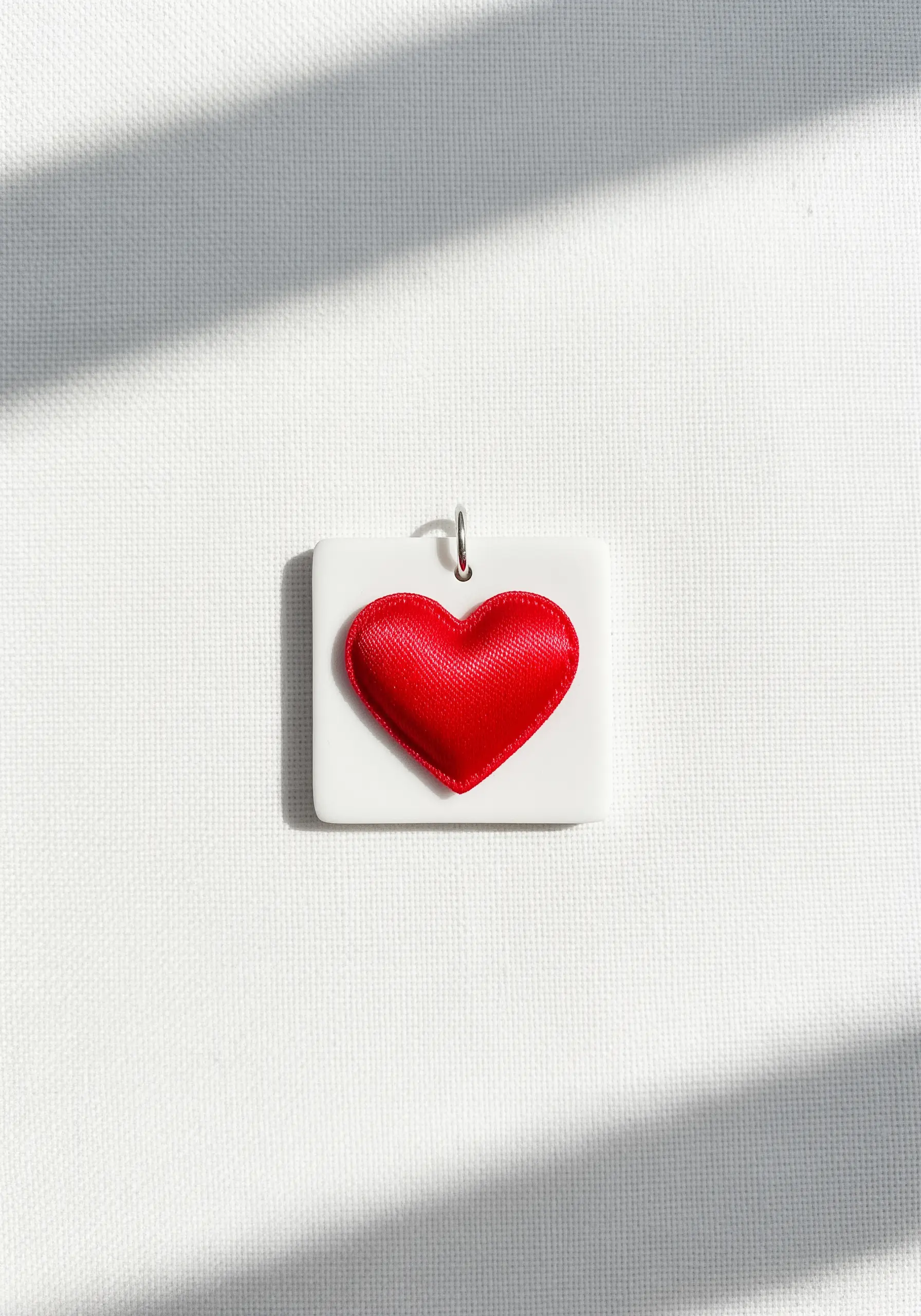 A padded red satin stitch heart mounted on a square white pendant.