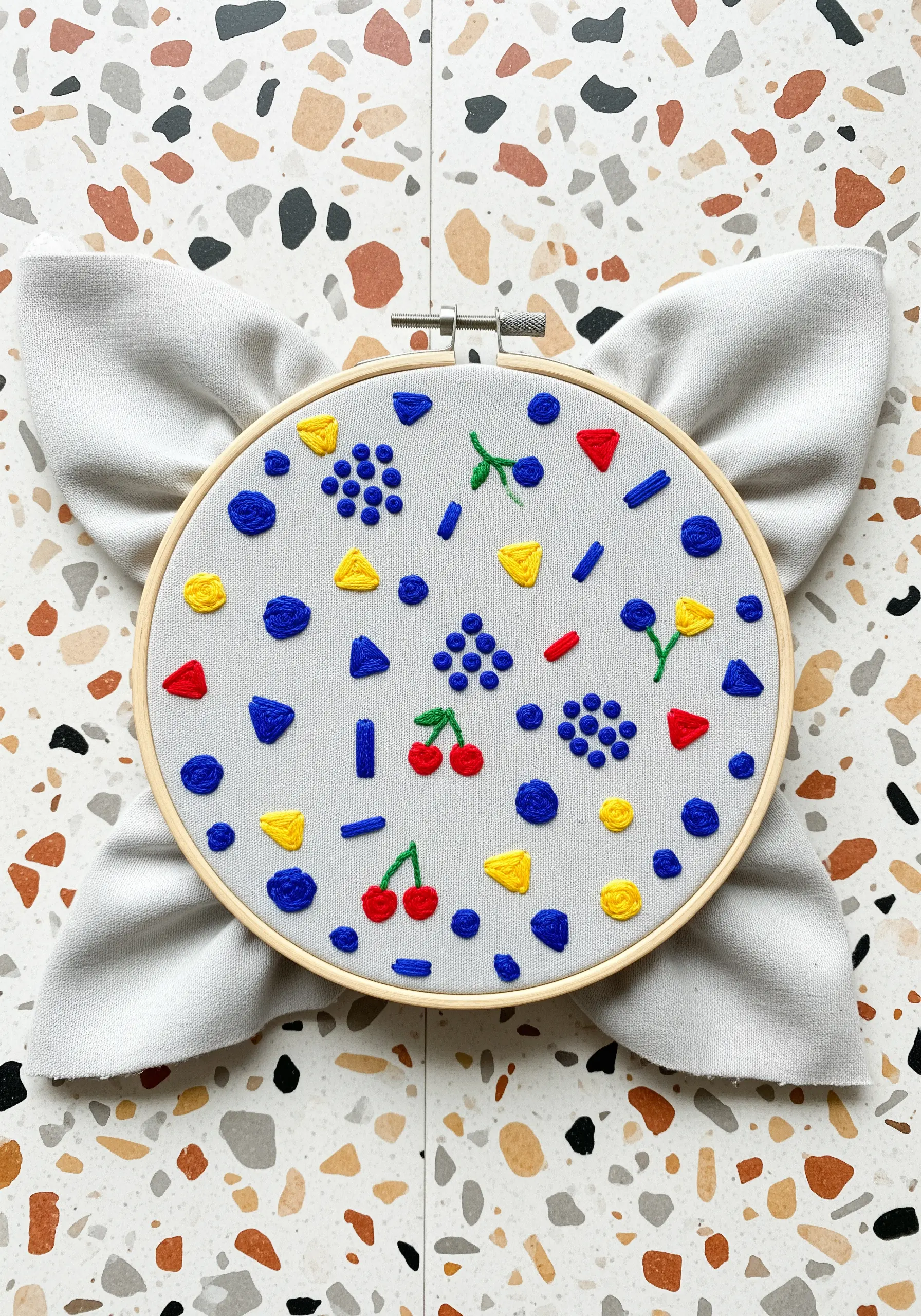 A playful pattern of small embroidered shapes and knots in red, yellow, and blue.