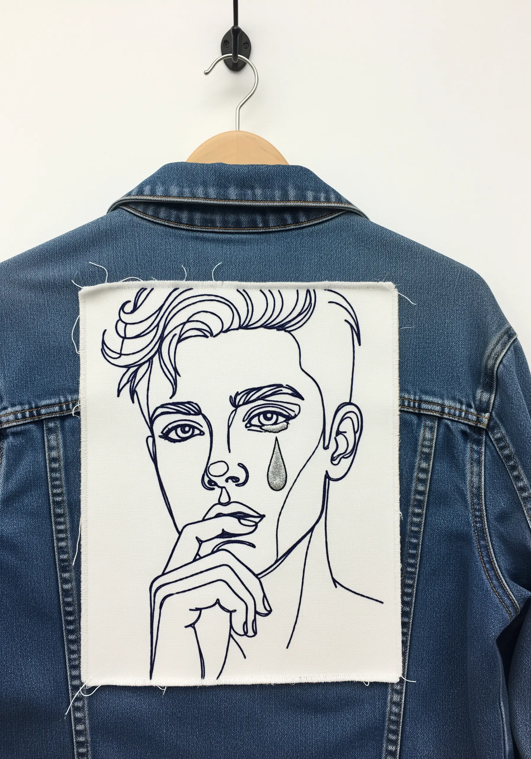 Line-art portrait embroidered on a frayed-edge patch on a denim jacket.