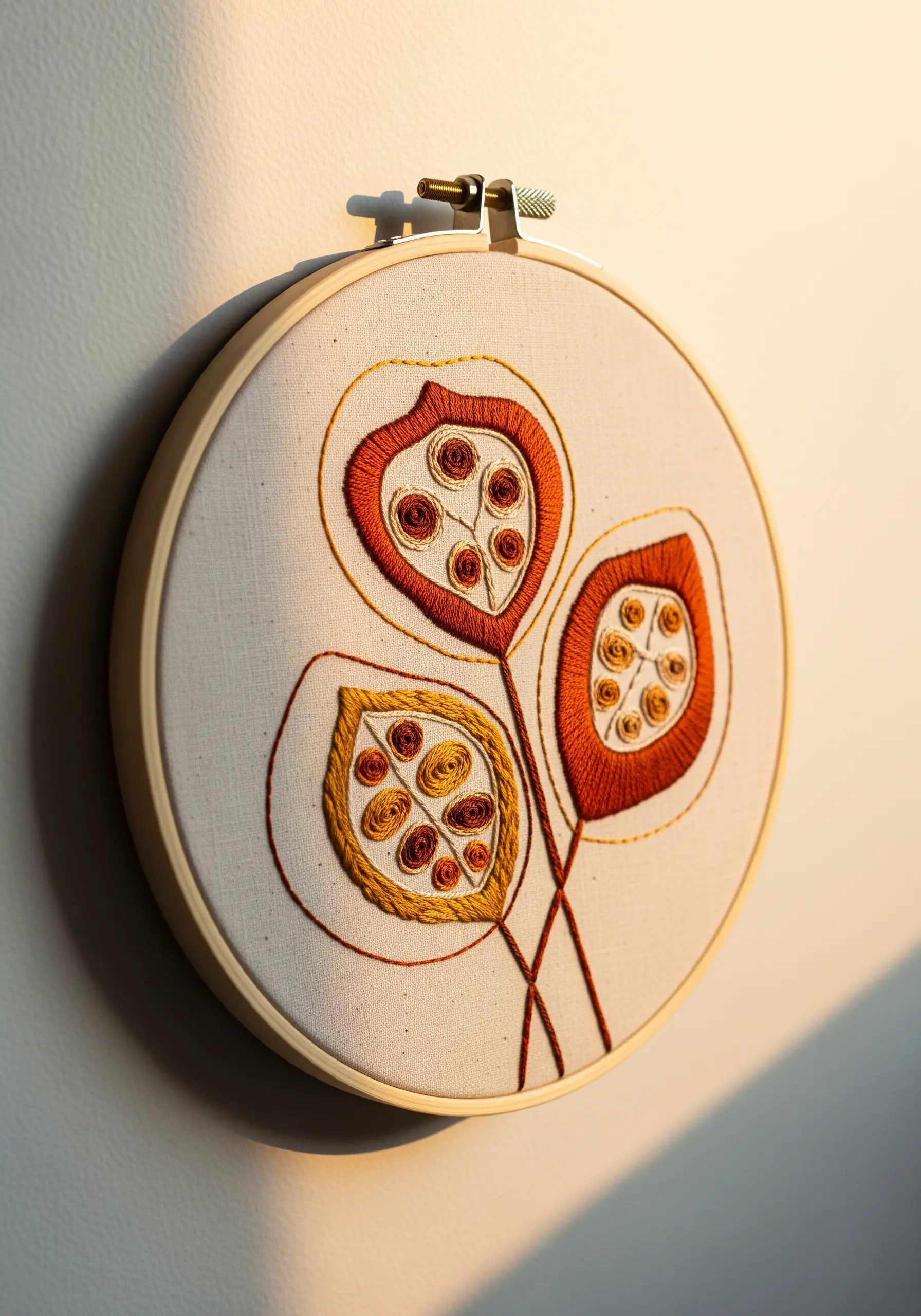 Three abstract embroidered seed pods in warm orange and yellow tones in a hoop.