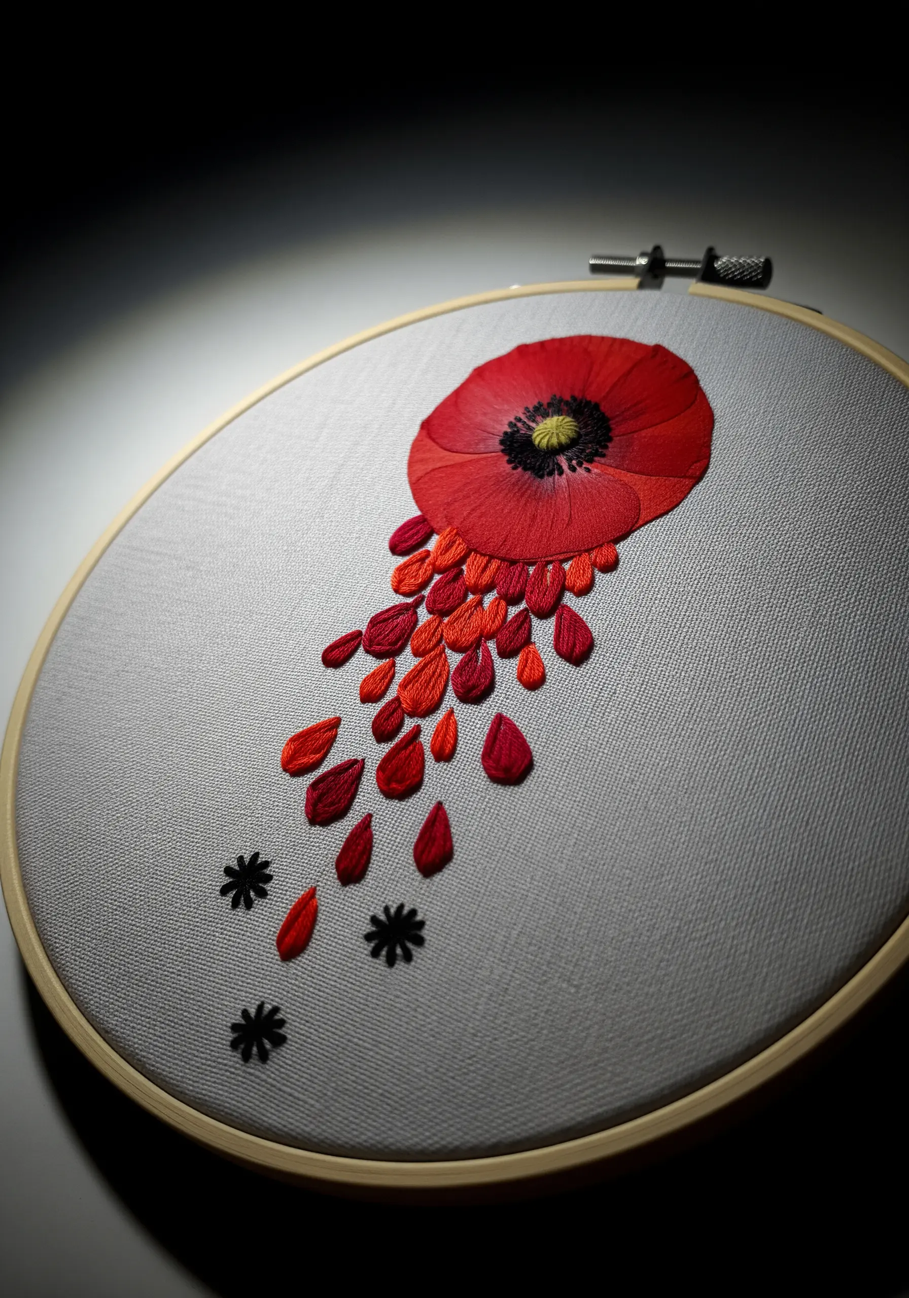 An embroidered red poppy with stitched petals cascading down the fabric in shades of red and orange.