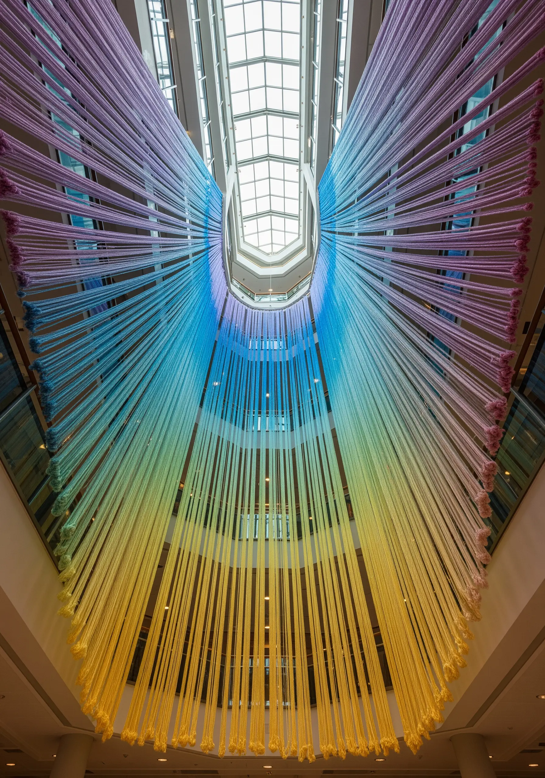 A wing-shaped installation of rainbow-colored ribbons stretching from a high ceiling down to a lower level.