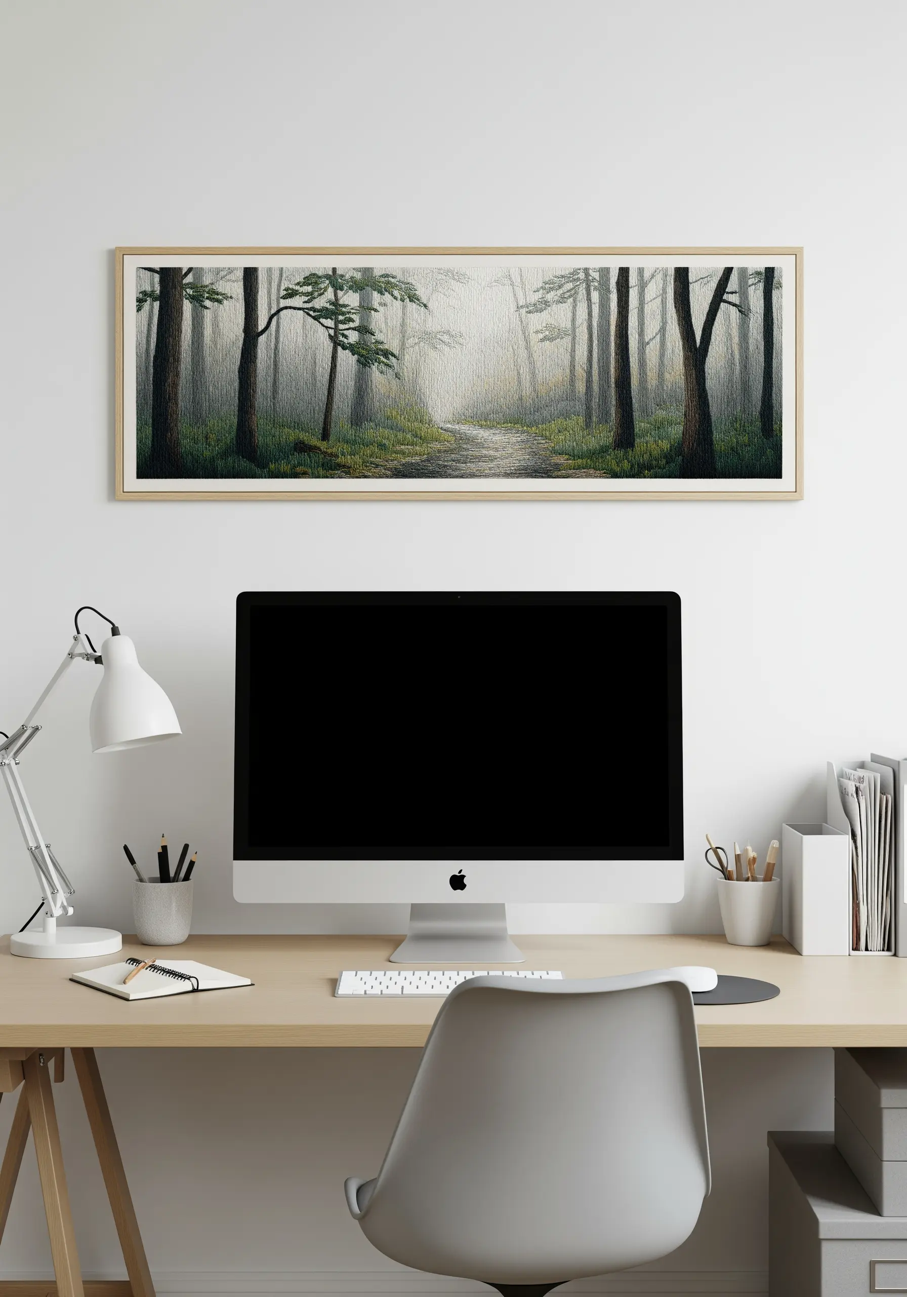A panoramic framed embroidery of a misty forest path above a home office desk.