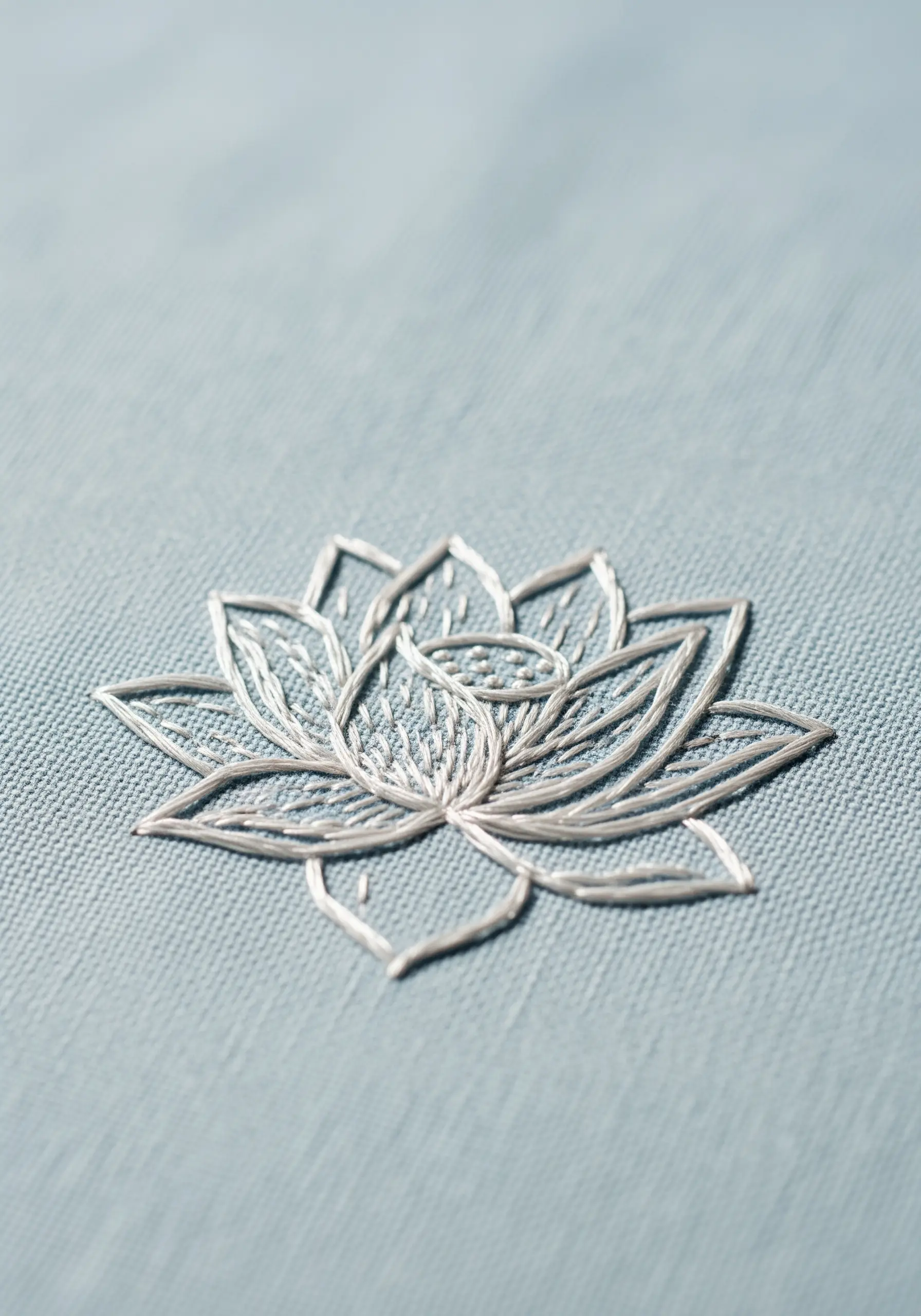 A white outline embroidery of a lotus flower on light blue fabric.