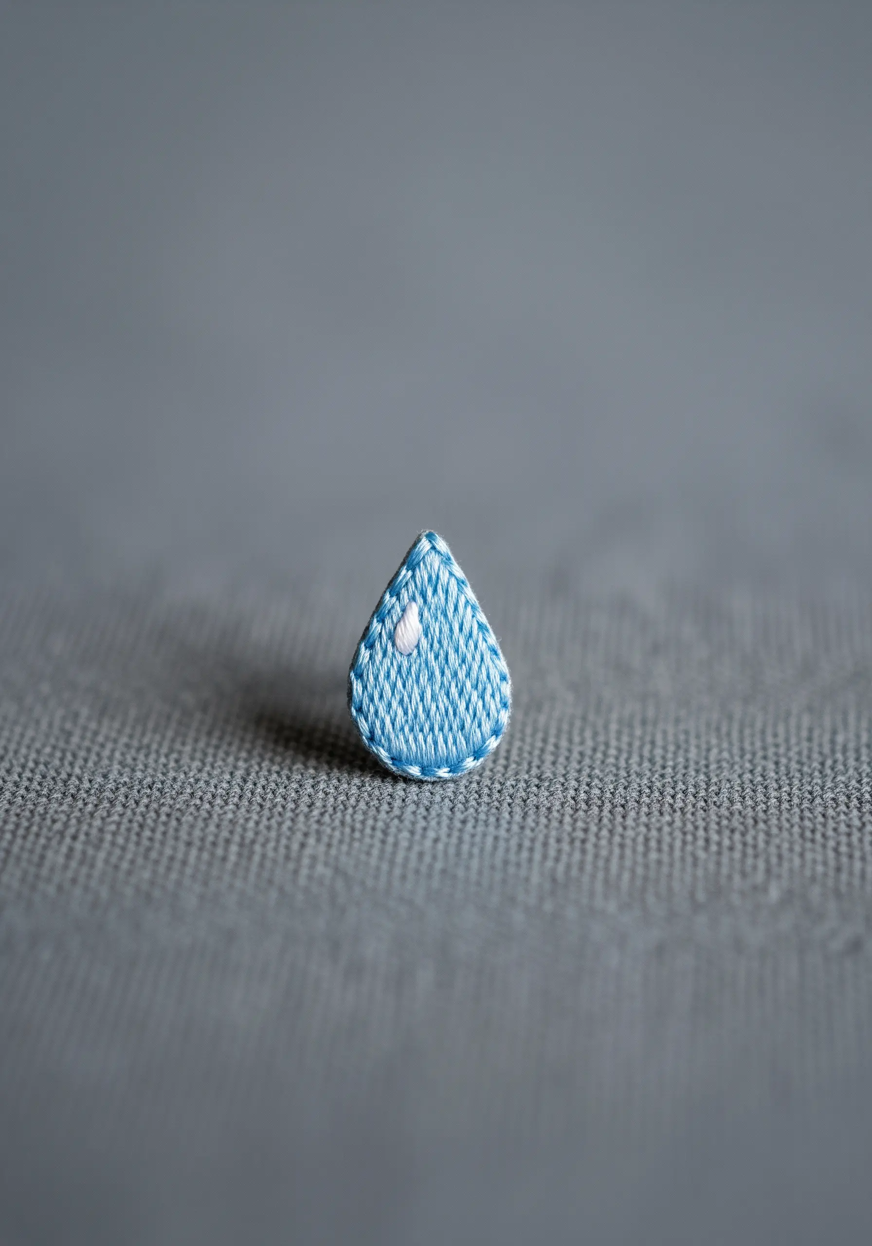 A tiny embroidered teardrop with blue satin stitch and a small white highlight.