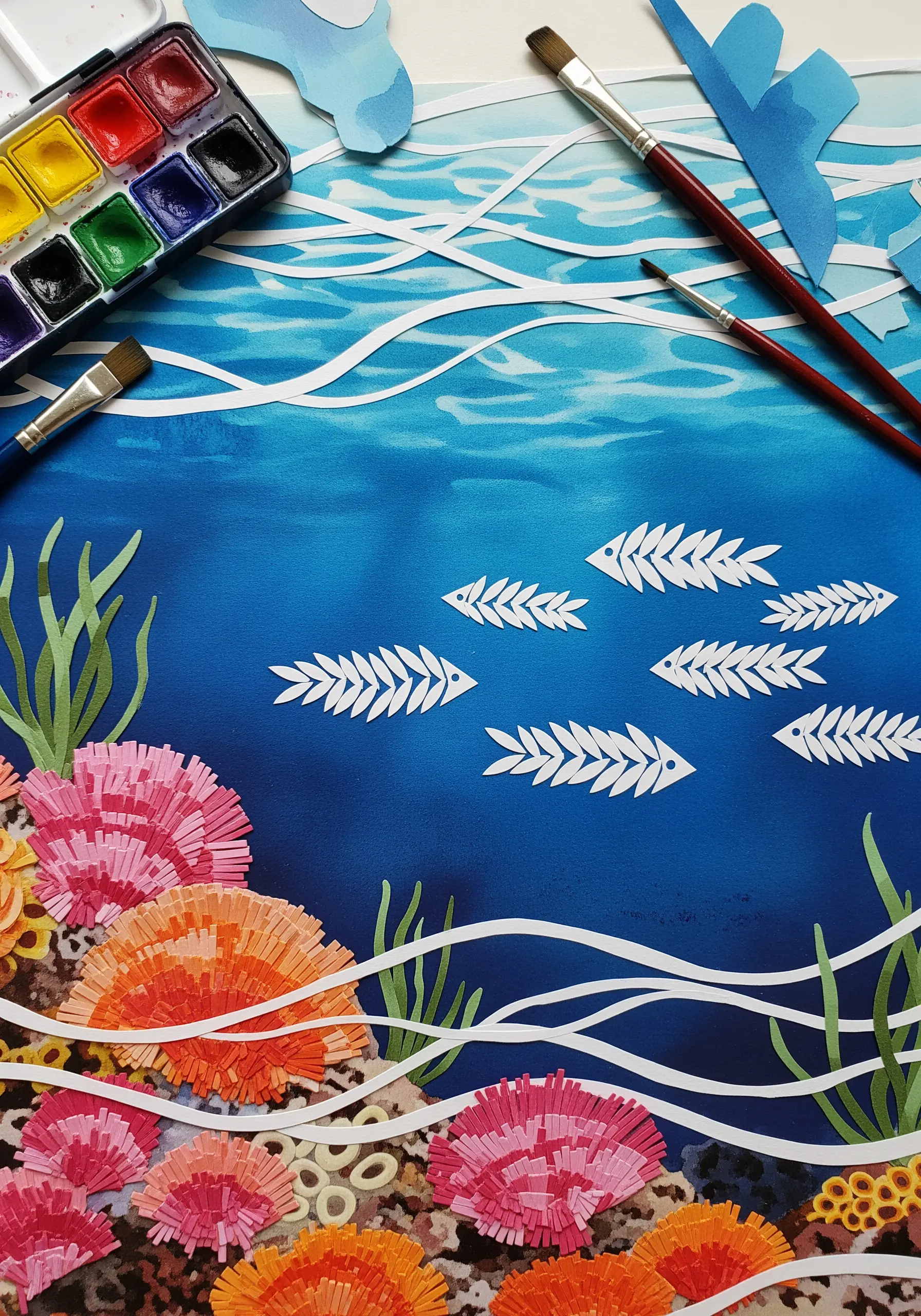 An underwater collage with fringed paper coral, watercolor background, and cut-out fish skeletons.