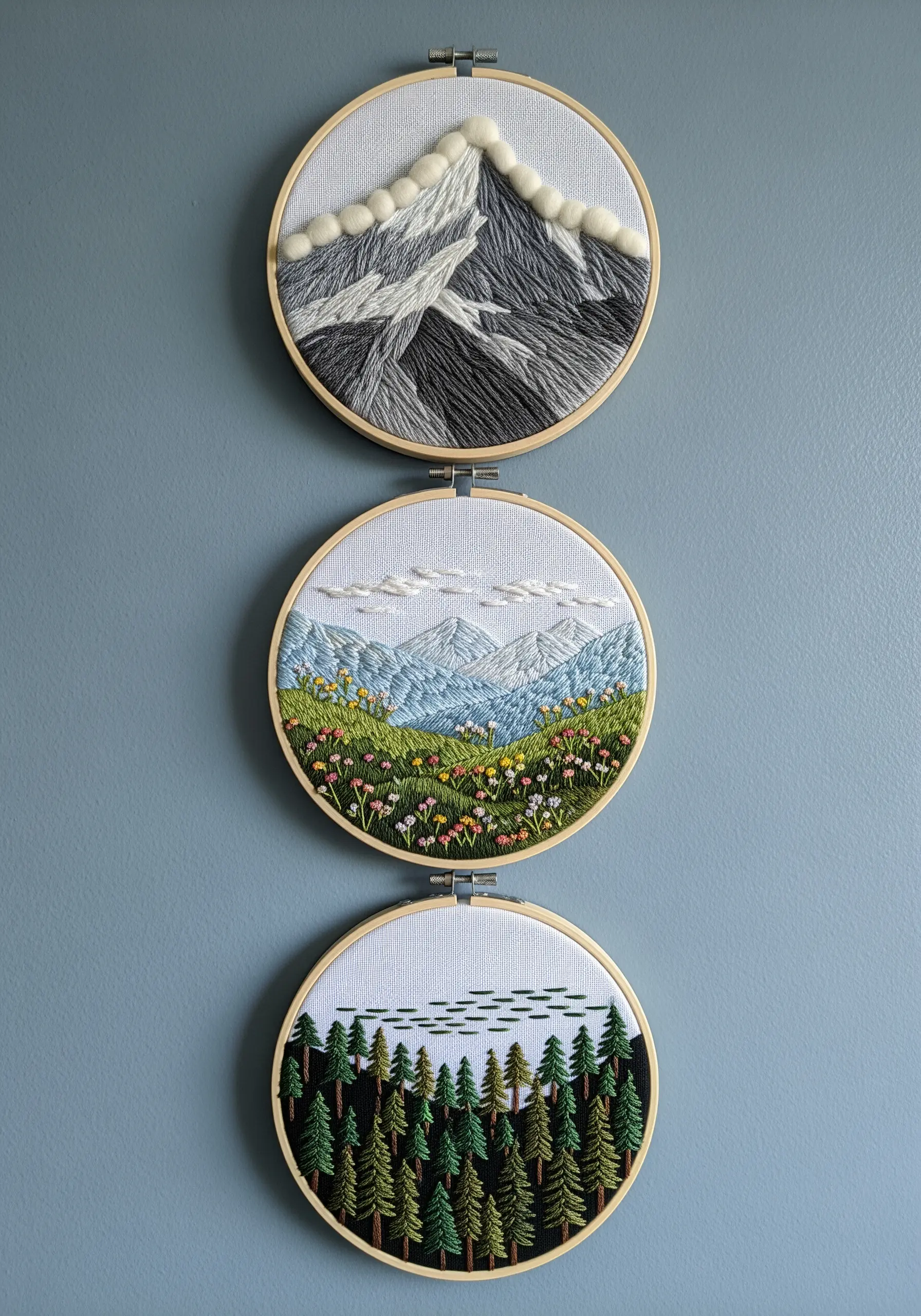 Landscape embroidery triptych with snowy mountains, a valley, and a forest.