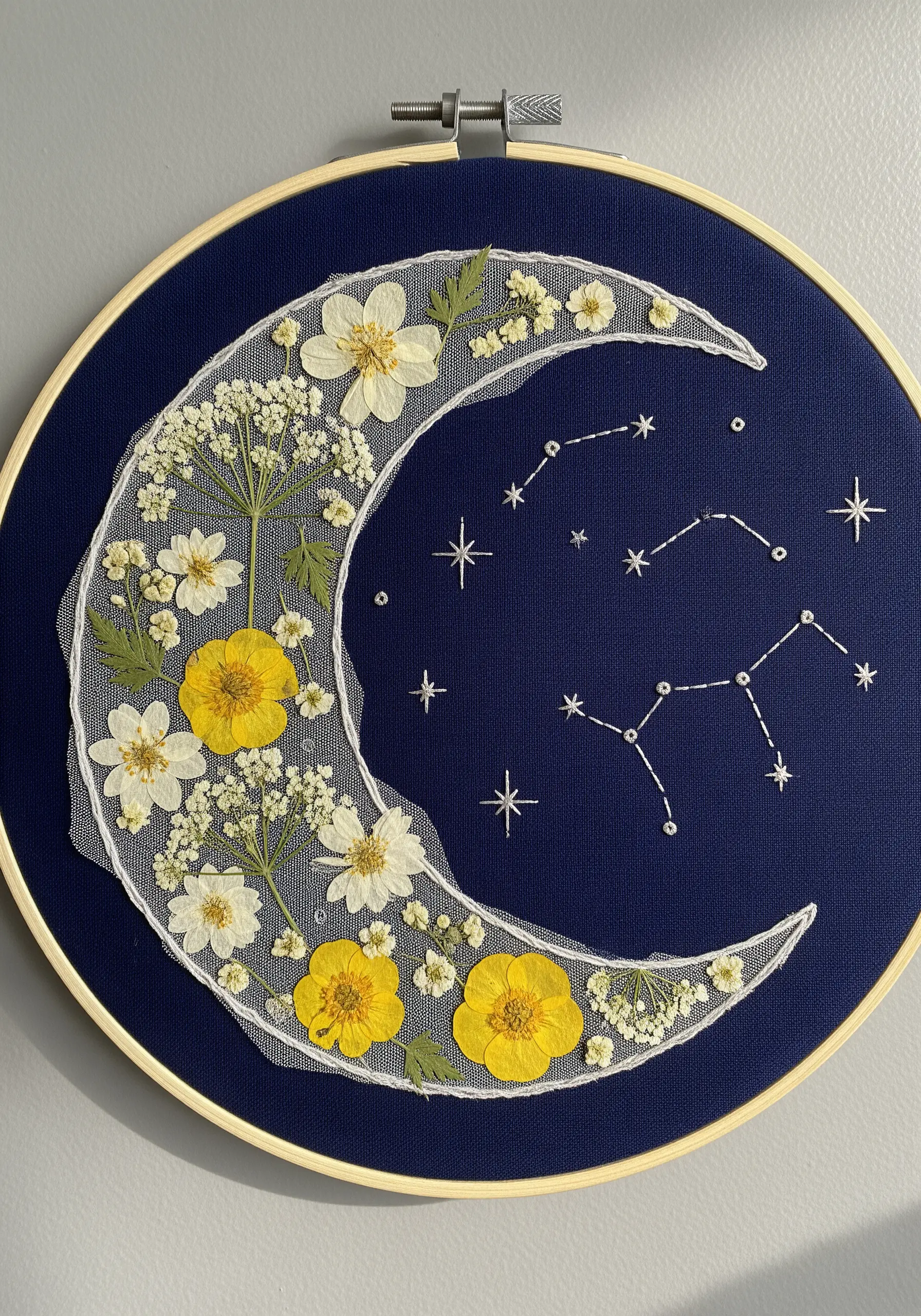 A crescent moon made of pressed flowers on tulle, appliquéd onto navy fabric with constellations.