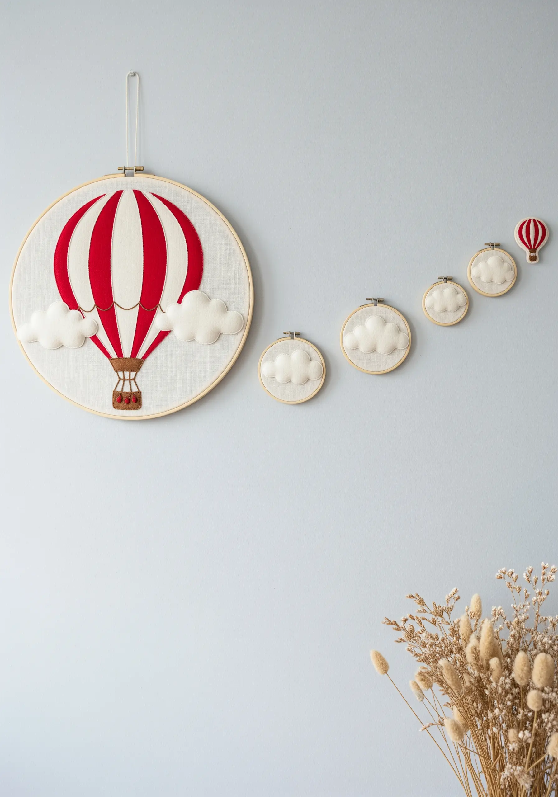 A large embroidery hoop with a red and white felt appliqué hot air balloon among puffy felt clouds.
