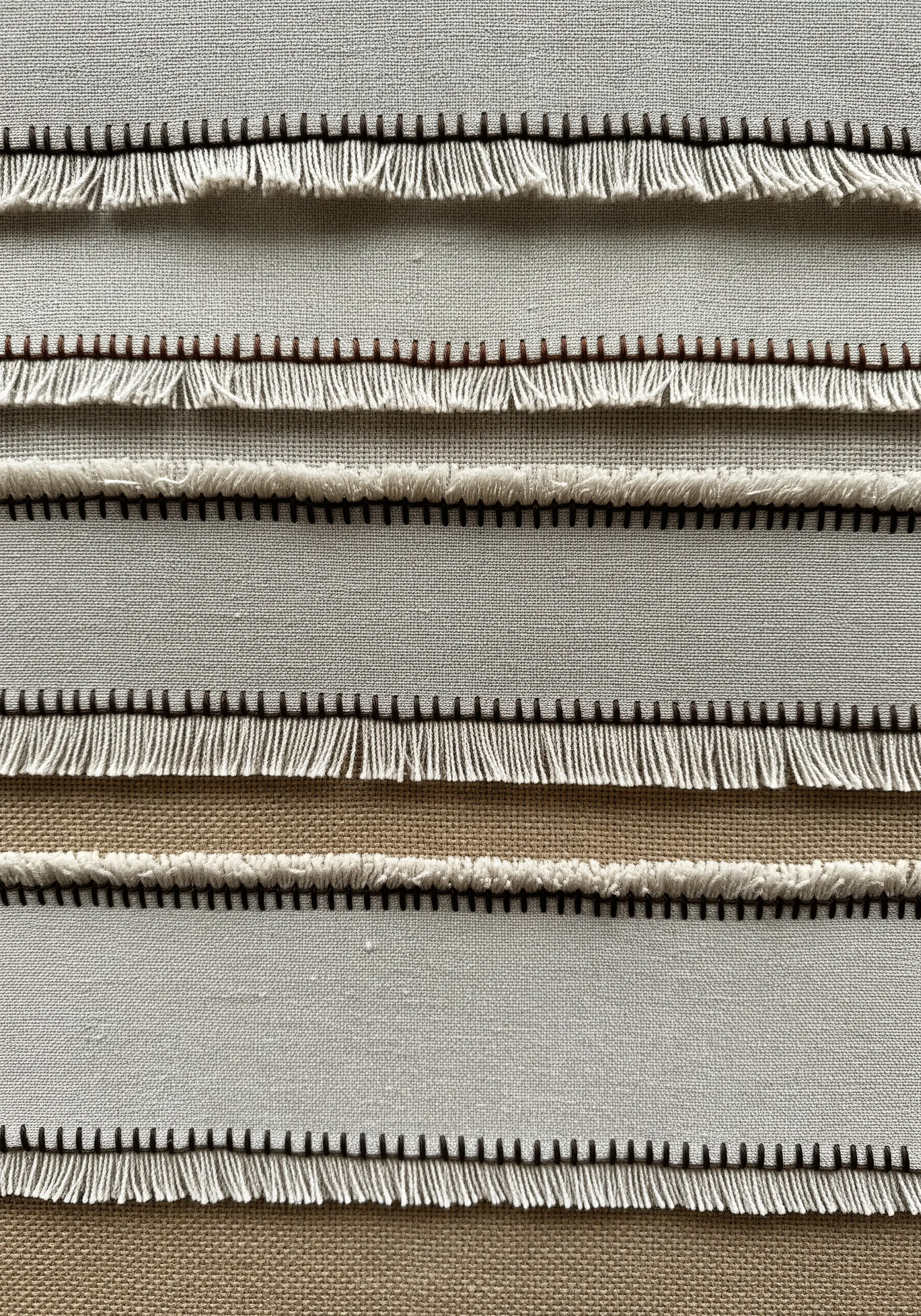 Layered strips of off-white fabric with frayed edges, secured with brown thread.