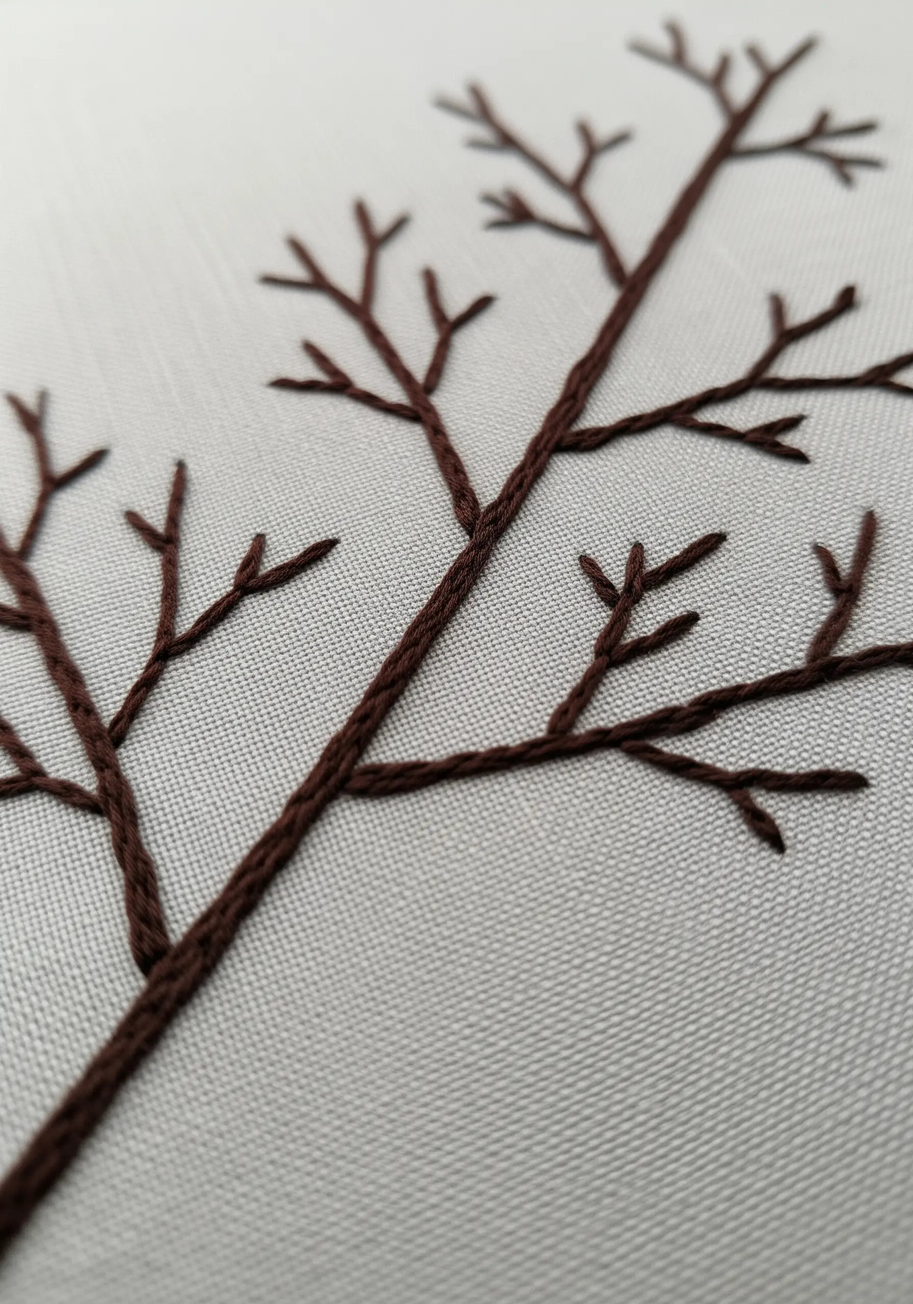 The silhouette of bare tree branches embroidered in brown thread on a light fabric.
