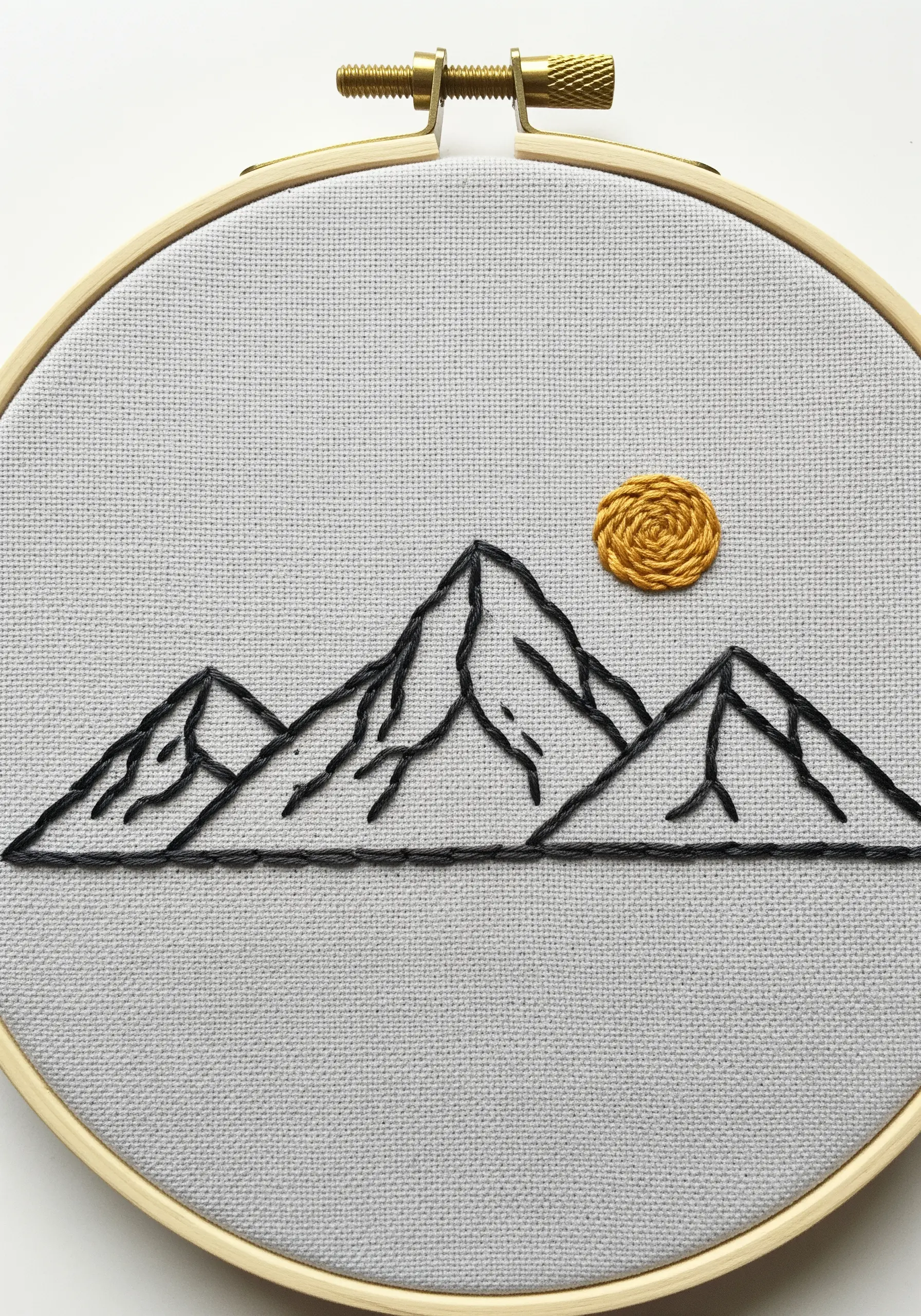 Minimalist mountain range outline in black thread with a woven yellow sun.