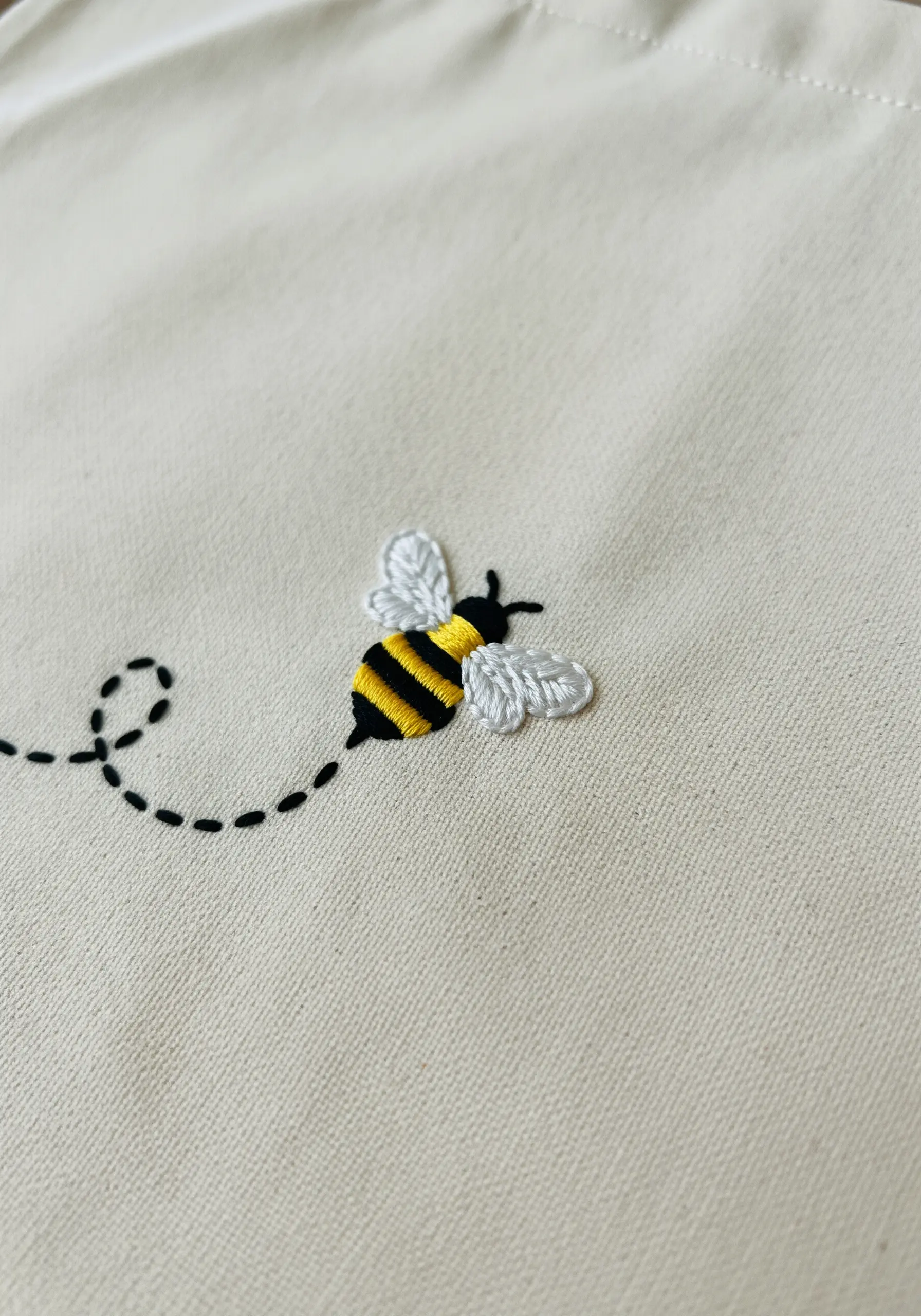 A small embroidered bee with a dimensional body and delicate wings, flying in a loop.
