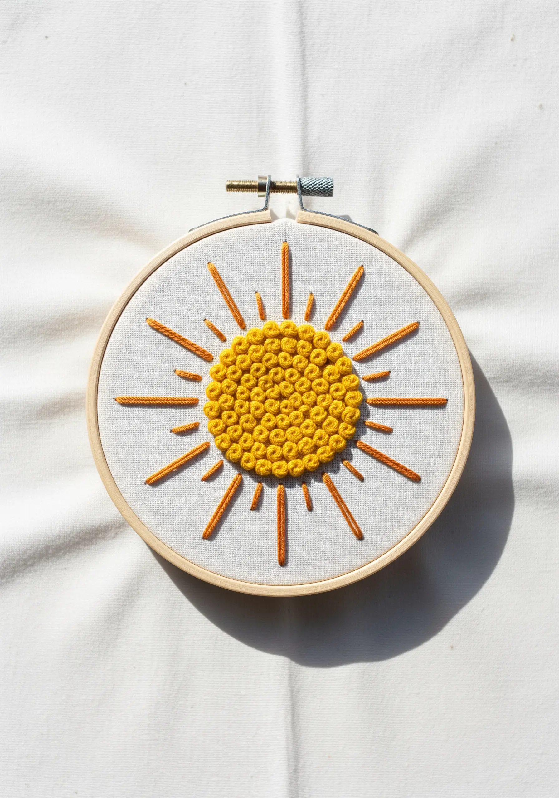 A stylized sun with a textured French knot center and smooth satin stitch rays.