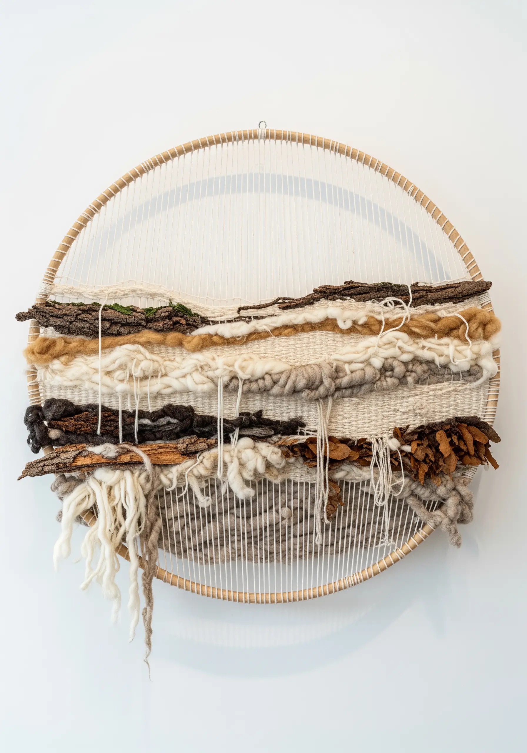 A circular weaving on a hoop loom featuring neutral-toned wool, bark, and other natural textures.