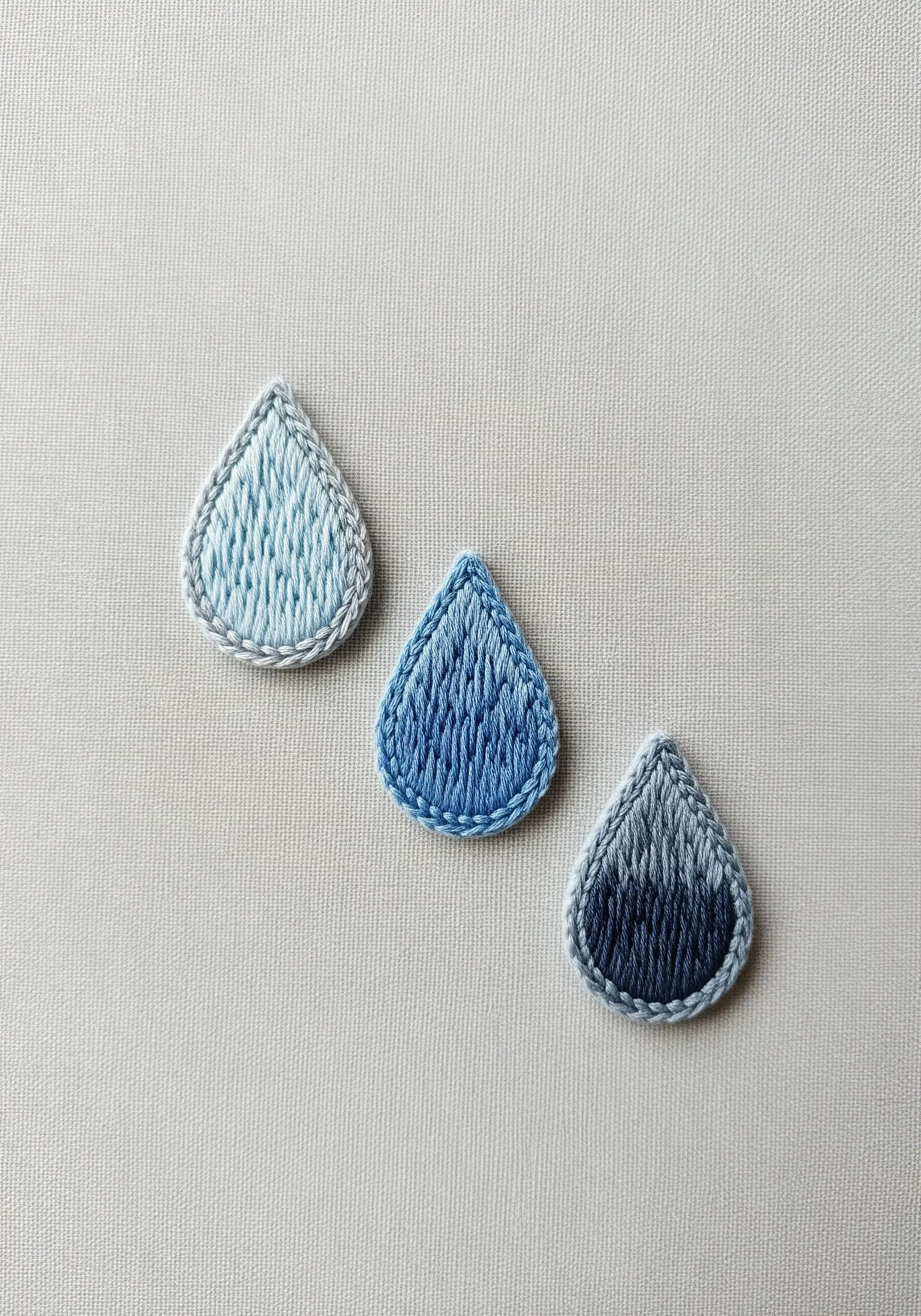 Three embroidered raindrops, each with a smooth color gradient from light to dark blue.