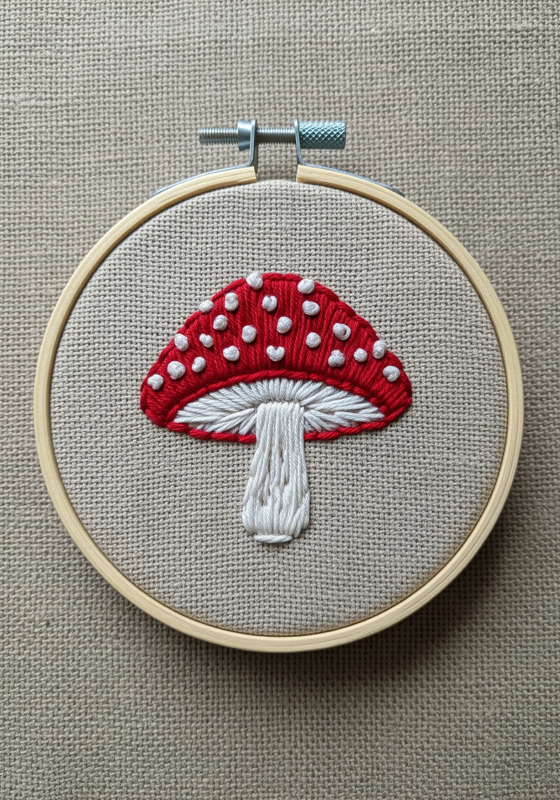 A red and white toadstool mushroom embroidered on neutral linen fabric.
