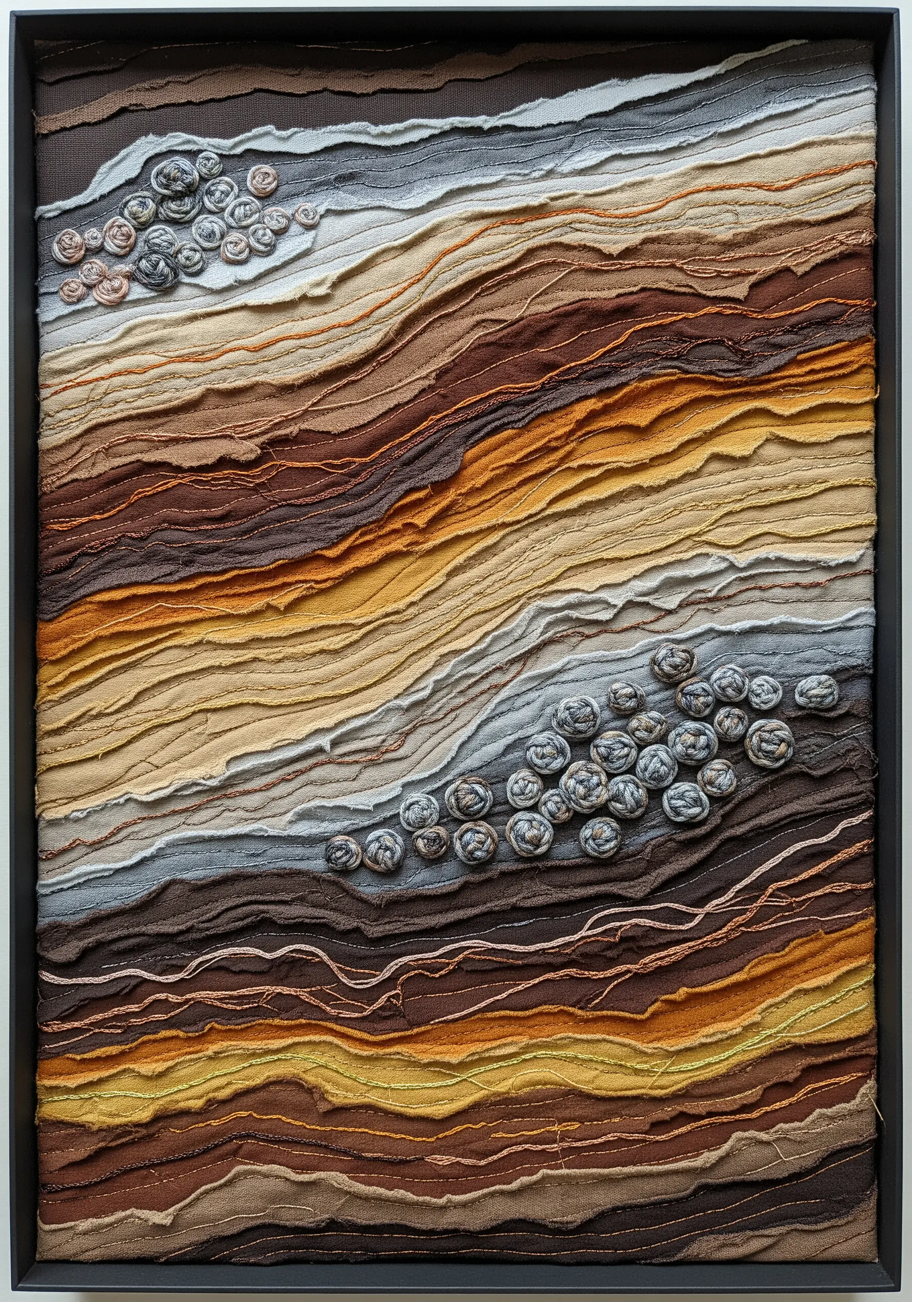 Framed textile art with layered, raw-edge earthy fabrics and clusters of woven buttons.