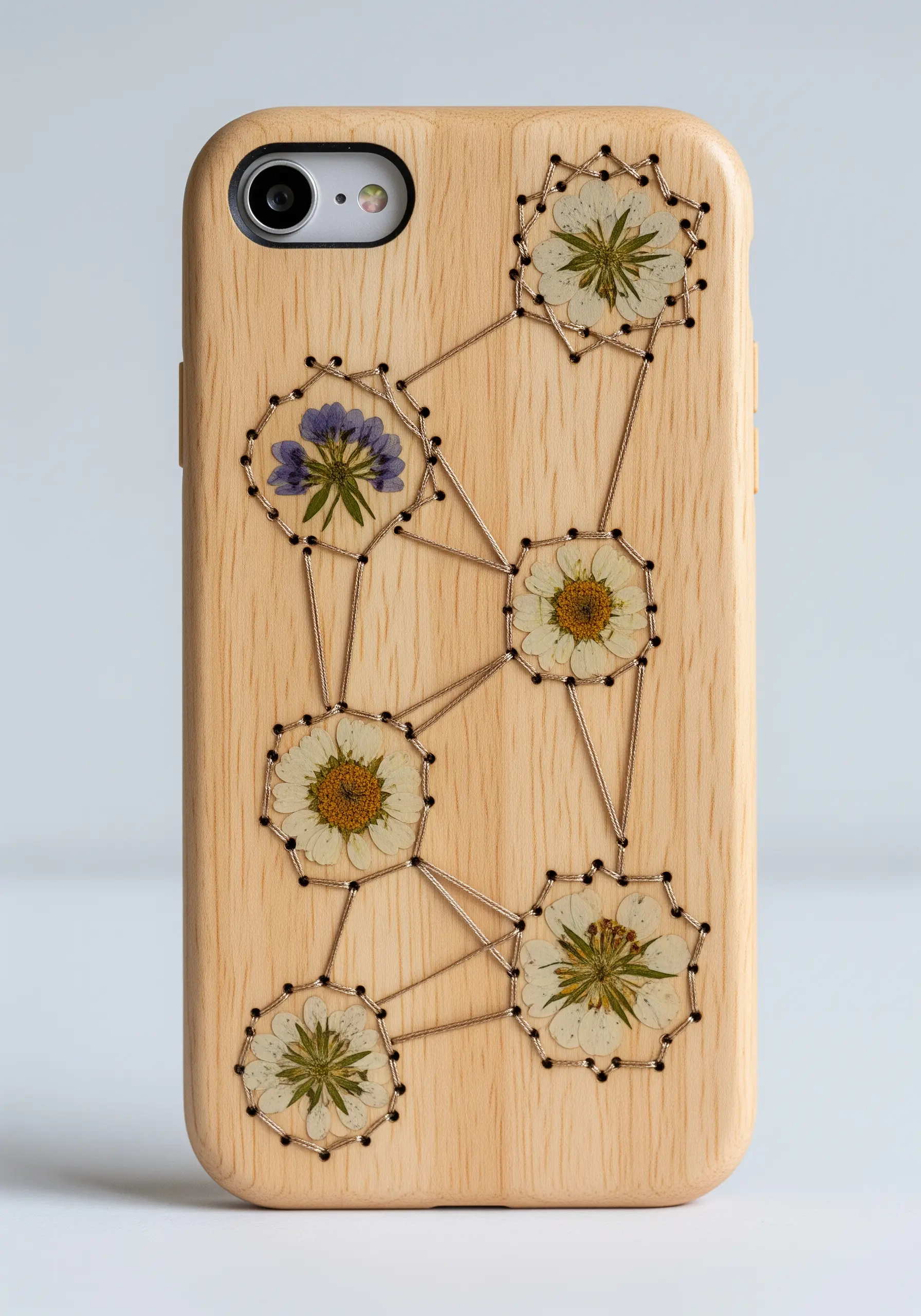 A wooden phone case decorated with pressed flowers connected by a geometric thread pattern.