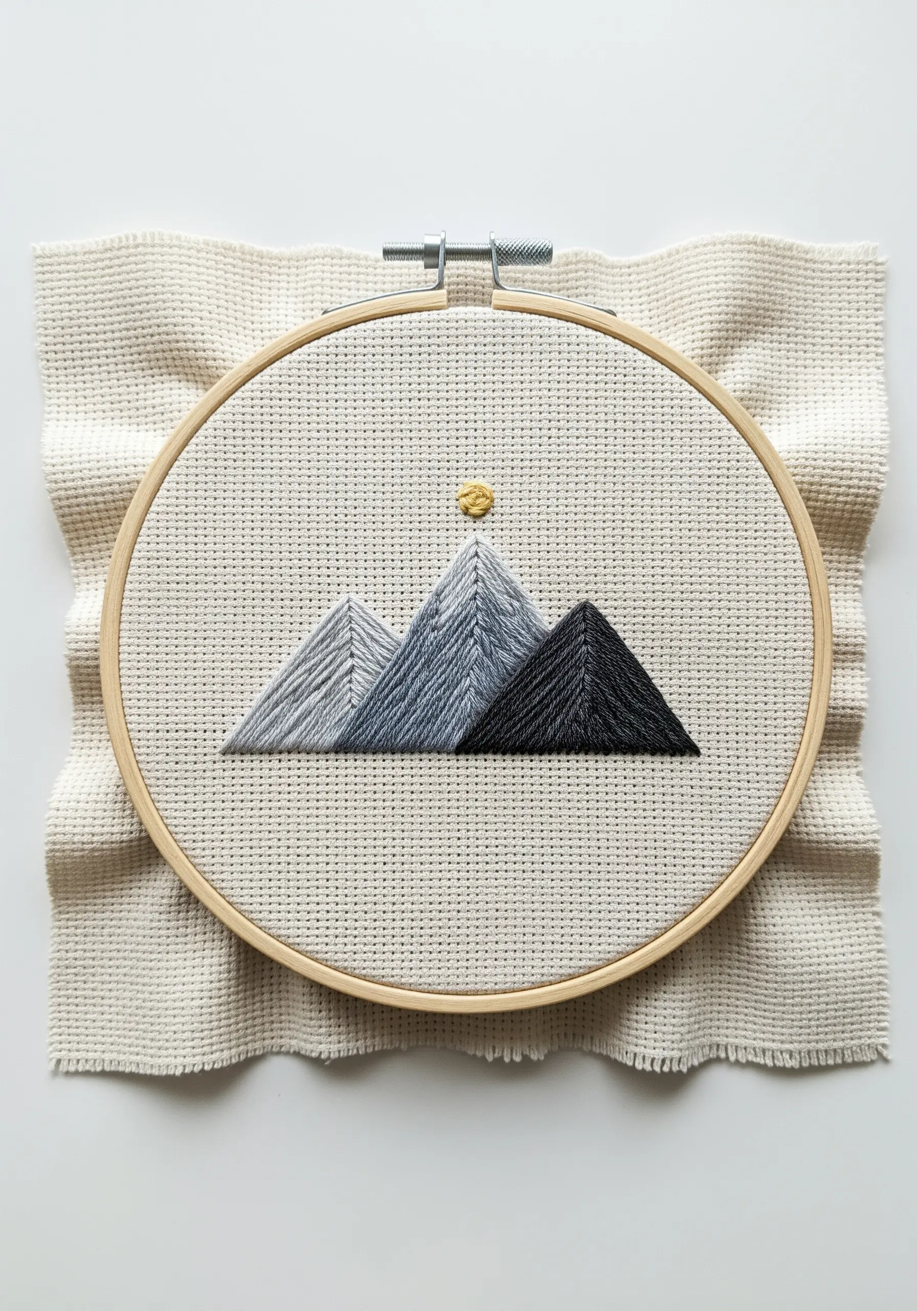Geometric mountain range with grayscale gradient stitching on Aida cloth in a hoop.