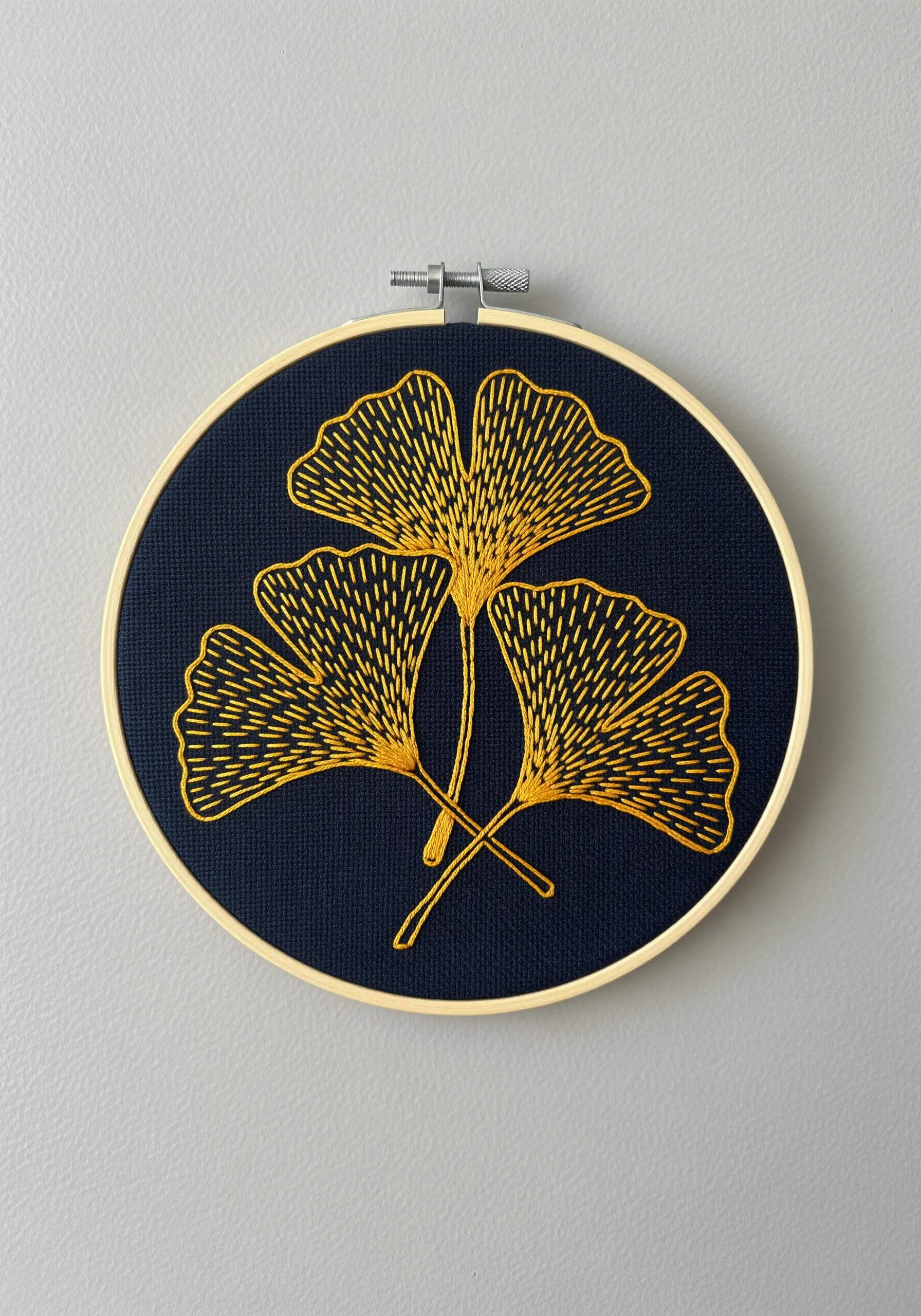 Three golden ginkgo leaves embroidered with radiating stitches on dark navy fabric.