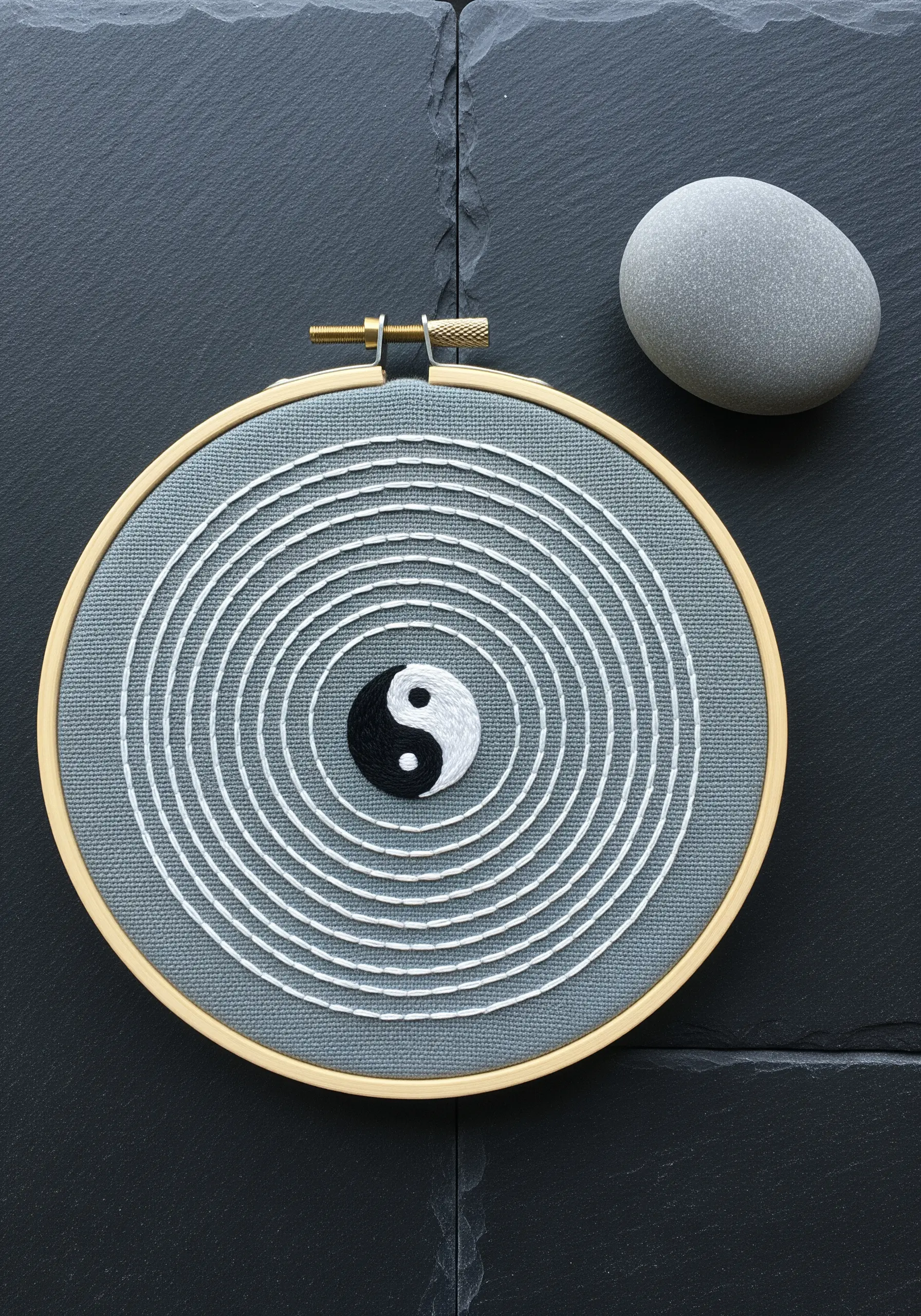 A yin-yang symbol at the center of a hypnotic spiral of white backstitch on gray fabric.