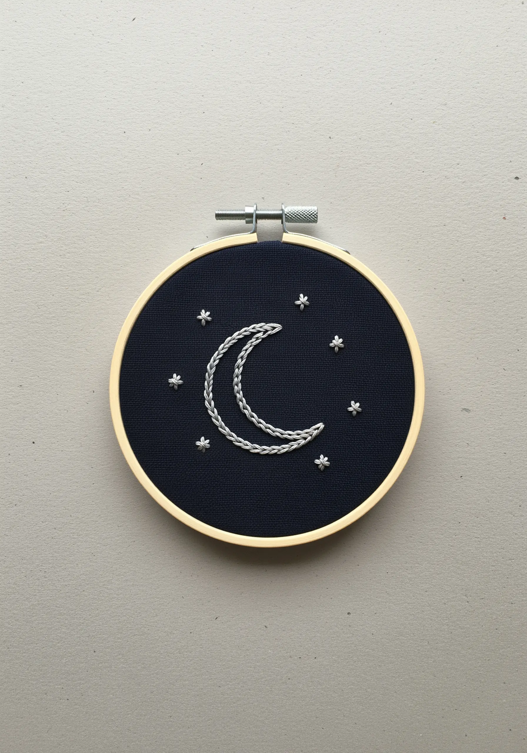 Crescent moon and stars embroidered with silver whipped chain stitch on dark navy fabric.