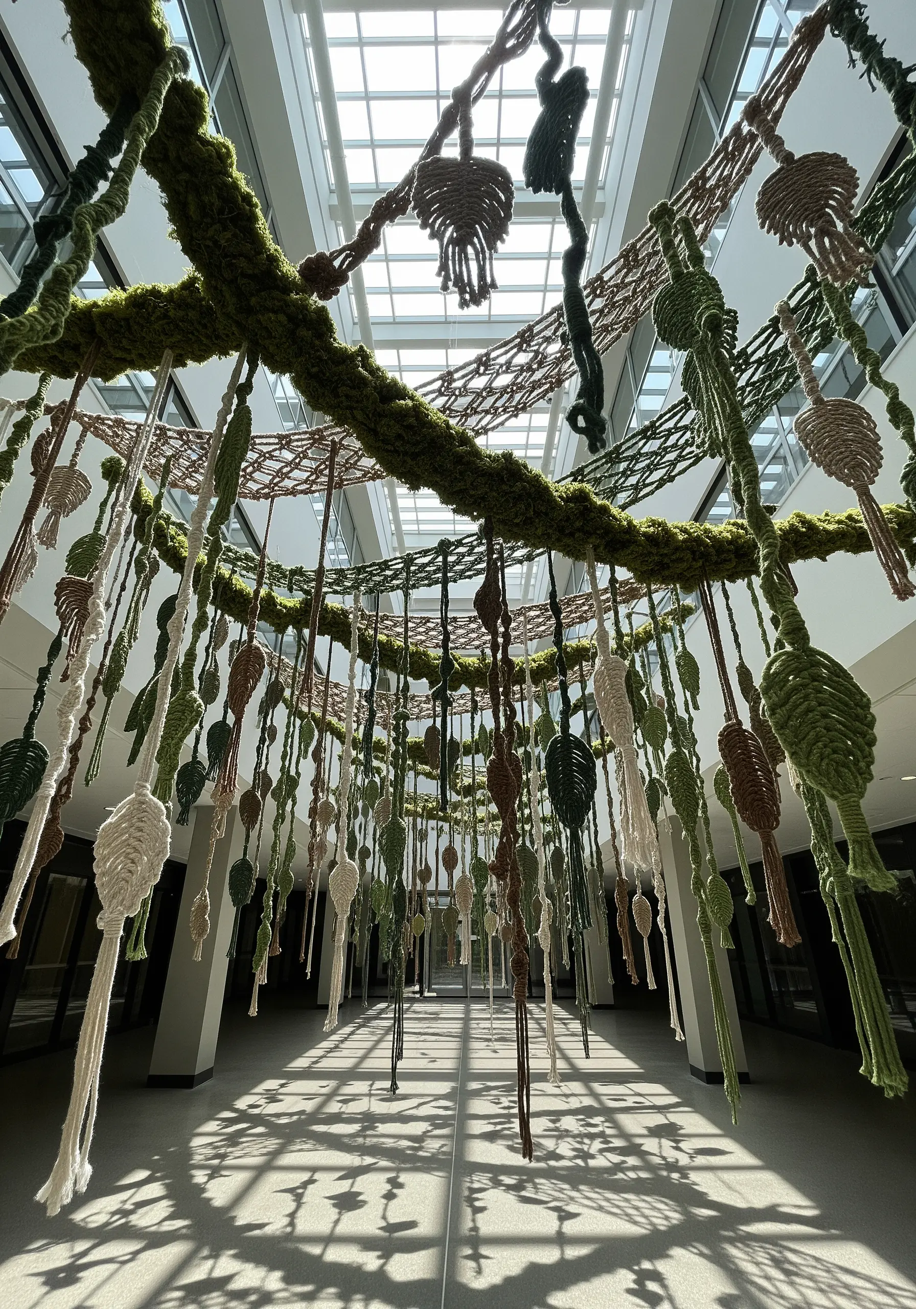 A ceiling installation of hanging macrame leaves in green, cream, and brown earth tones.