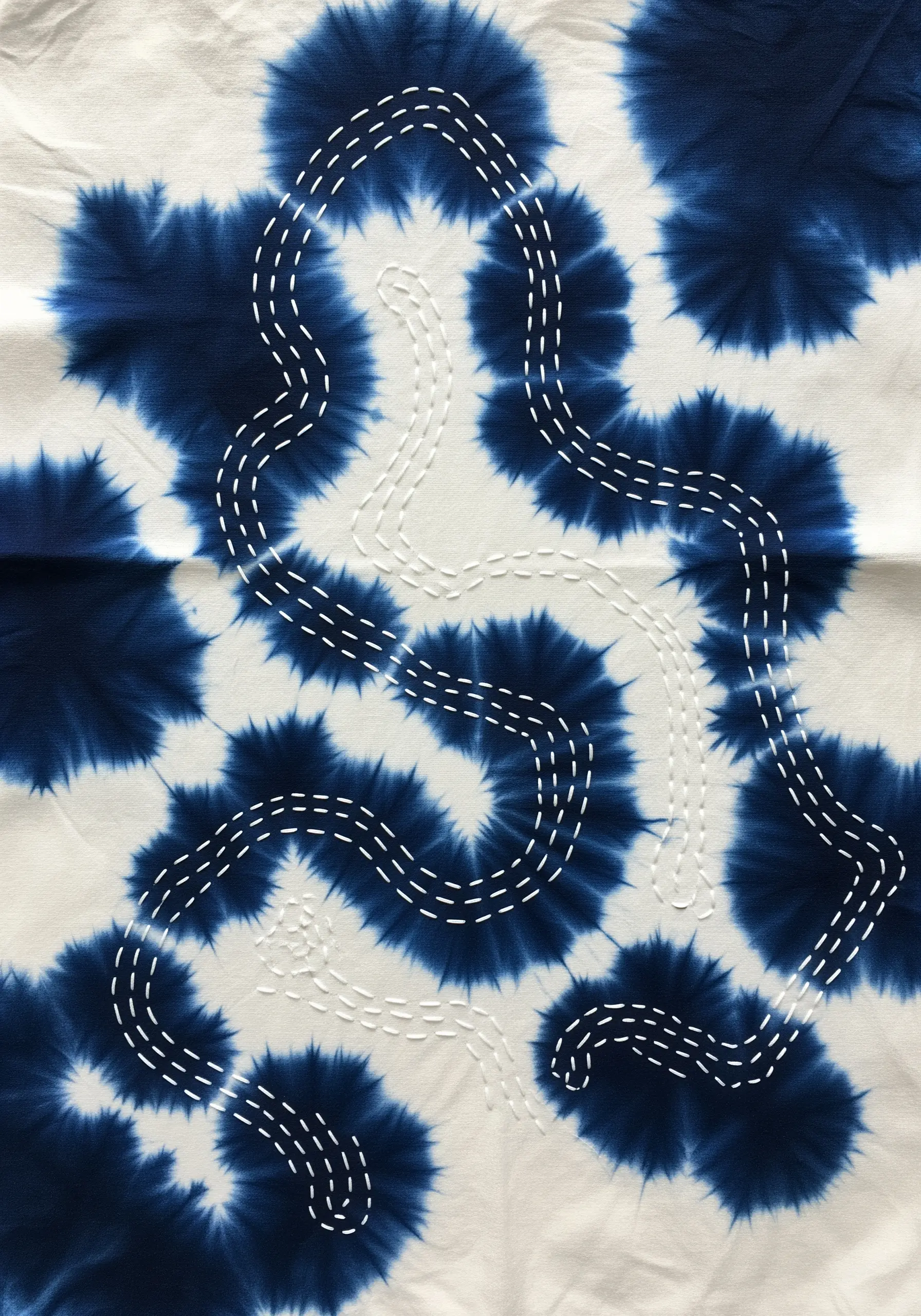 White running stitches create a winding path over a blue and white tie-dyed fabric.