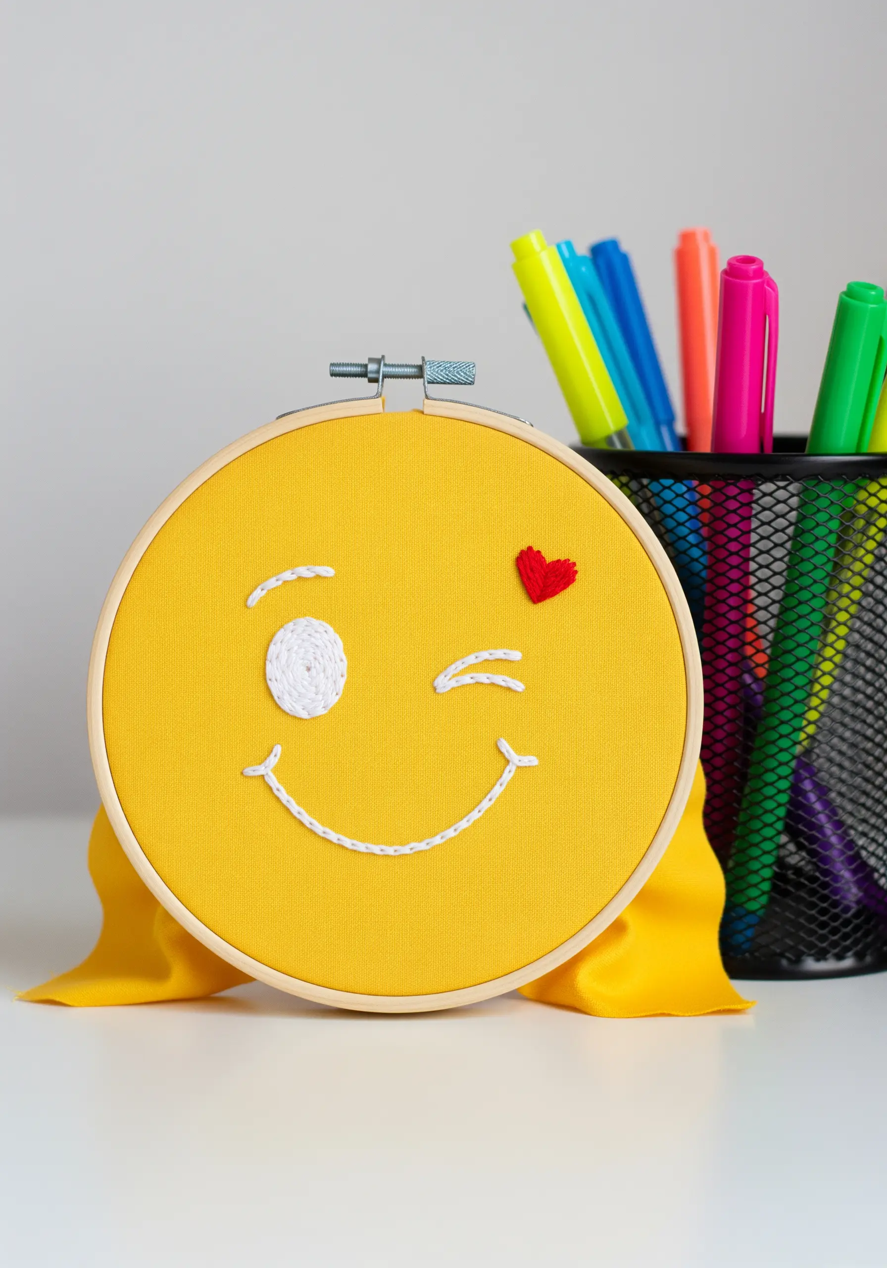 Winking emoji face with a dimensional woven wheel stitch for the open eye.