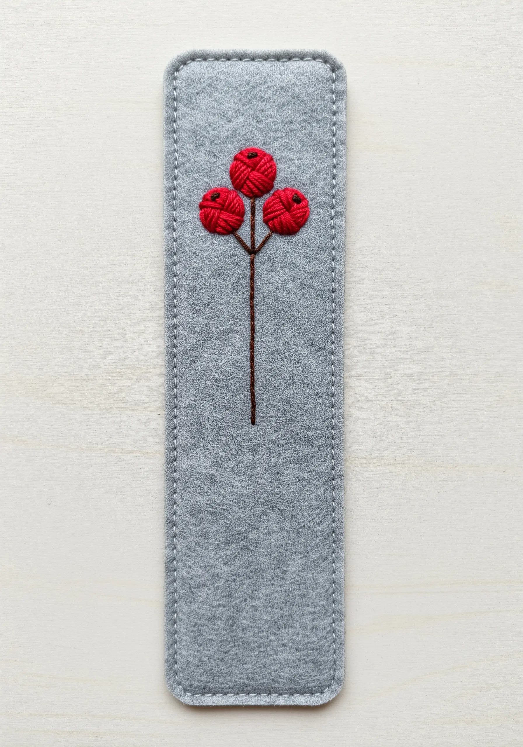 Three-dimensional red berries made with woven wheel stitch on a gray felt bookmark.