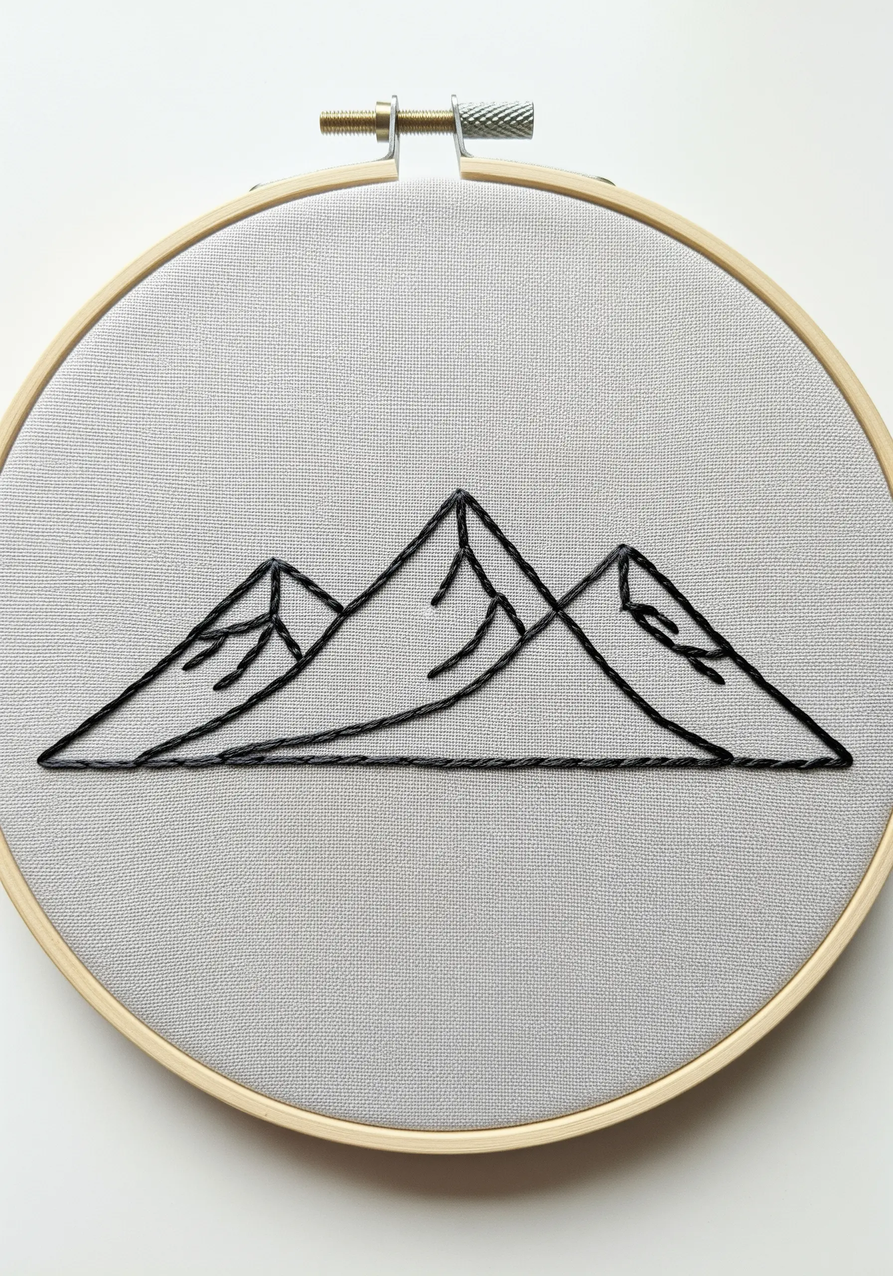 Minimalist black outline embroidery of three mountain peaks on gray fabric in a hoop.