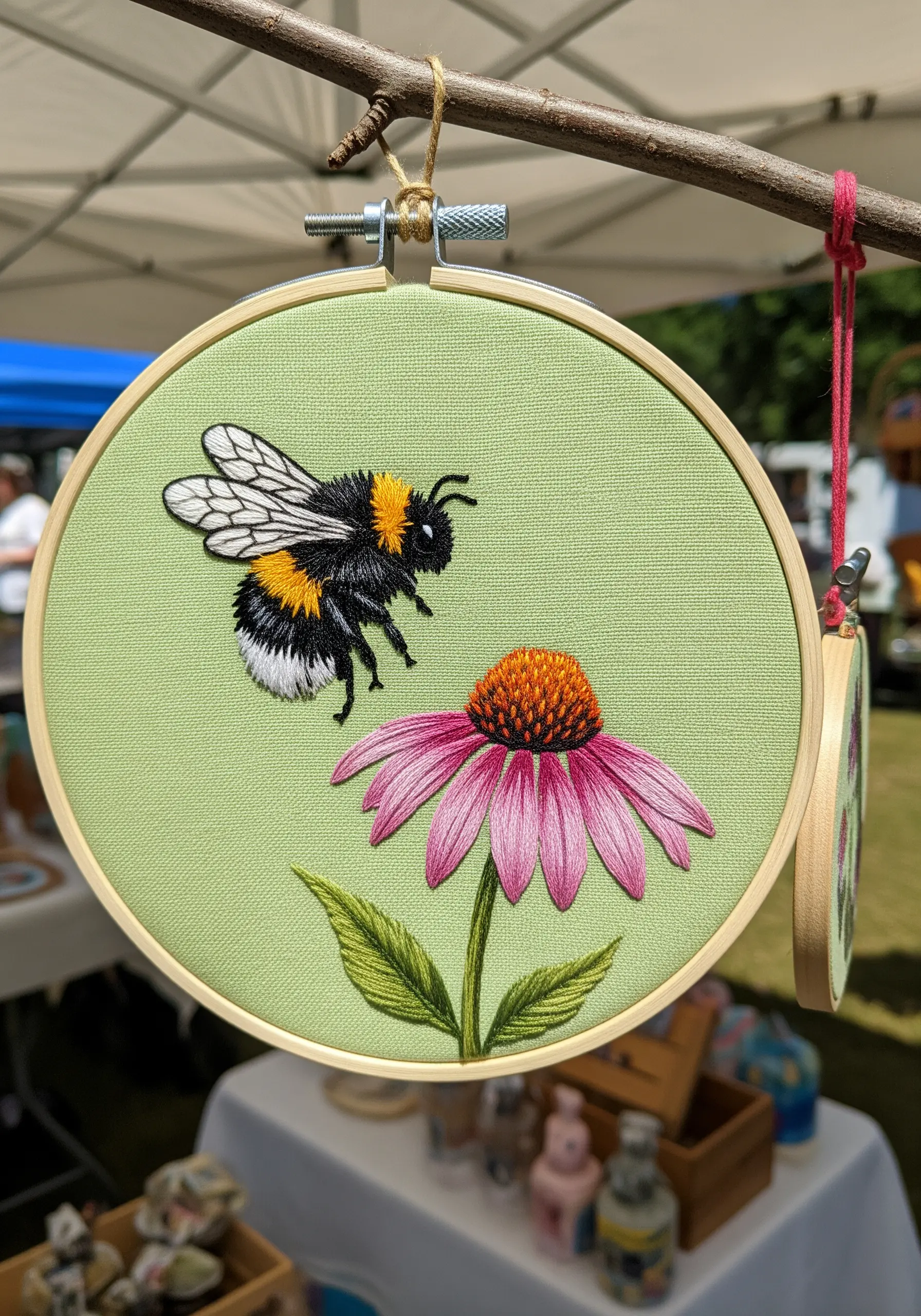 A highly detailed embroidery of a bee flying over a pink coneflower.