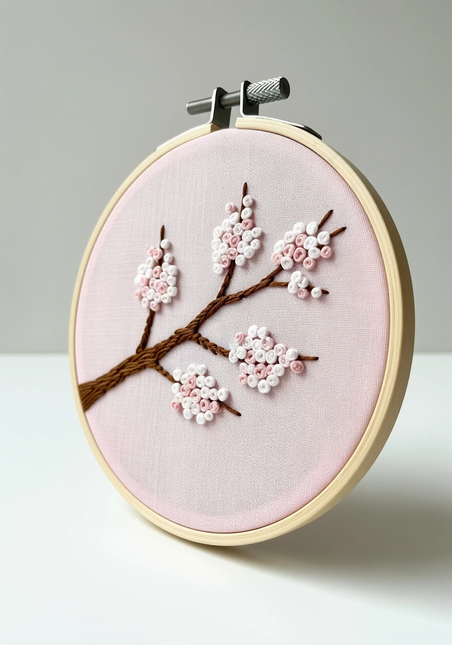 A cherry blossom branch embroidery with pink and white French knot flowers on light pink fabric.