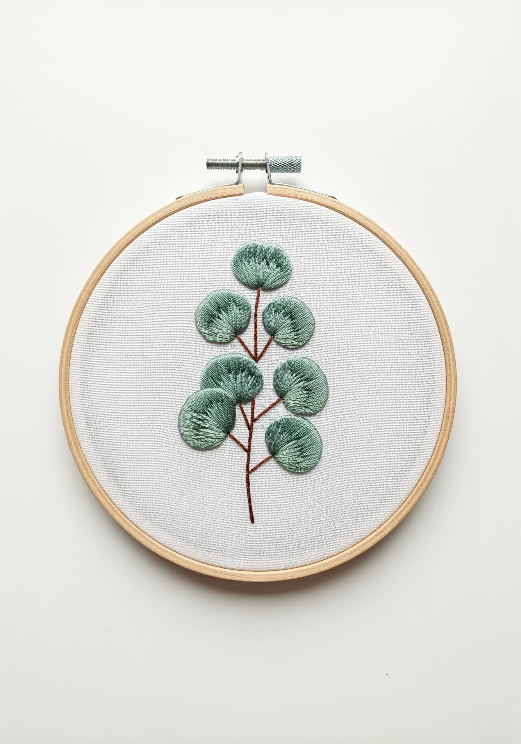 A silver dollar eucalyptus branch embroidered with fishbone stitch in a wooden hoop.