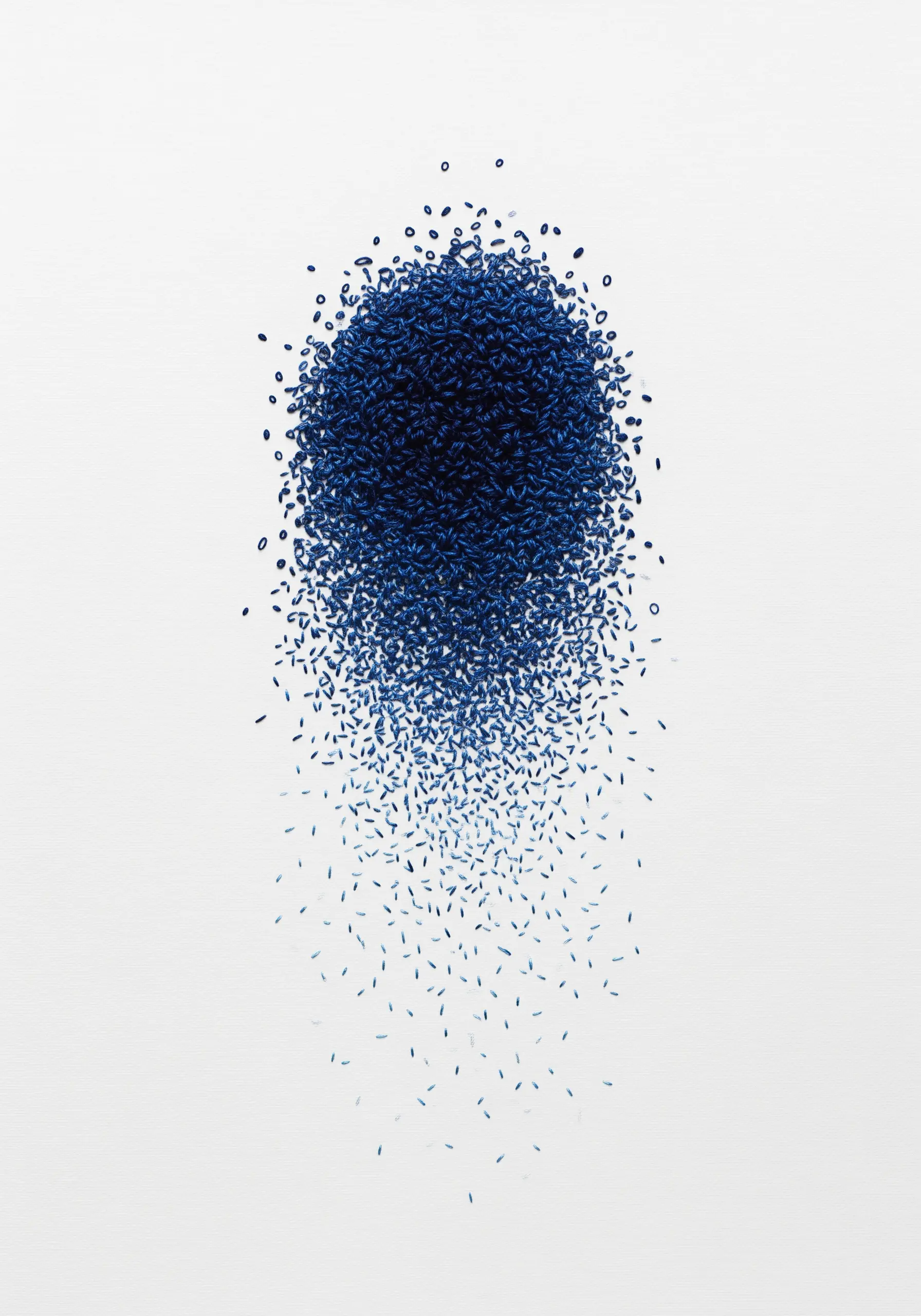 Abstract embroidery of a dissolving circle made of tiny blue seed stitches on white fabric.