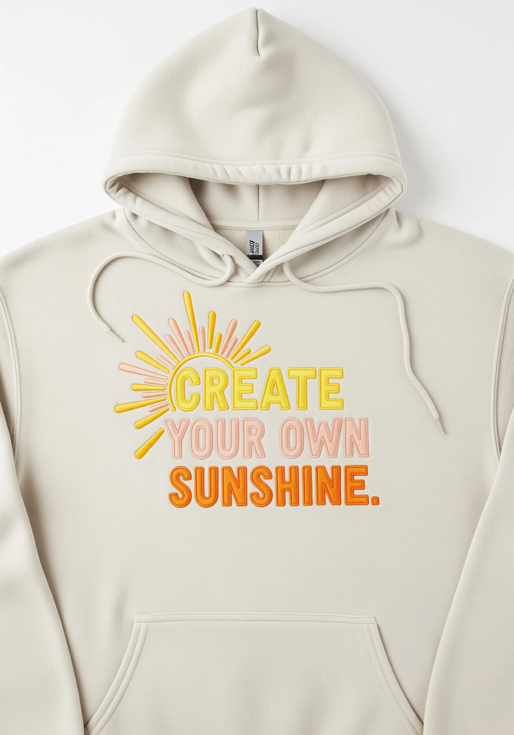 Embroidered quote 'Create Your Own Sunshine' in warm gradient colors on a cream hoodie.