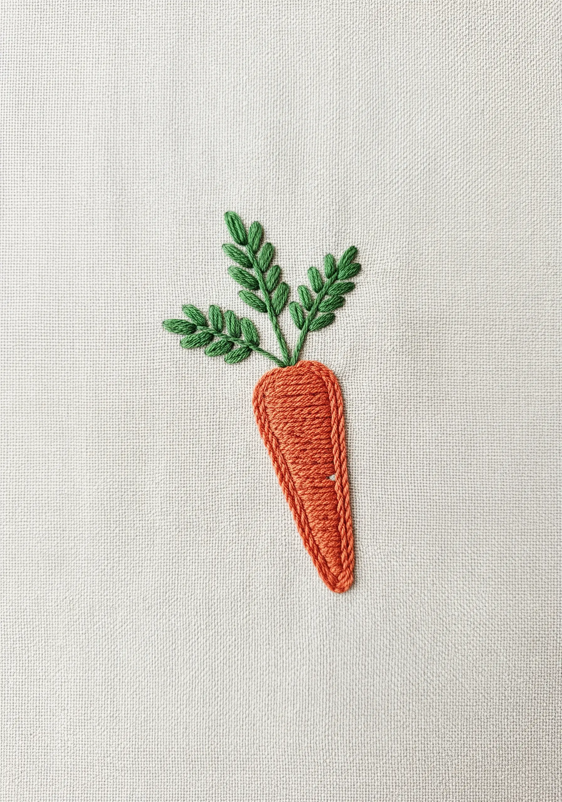 A hand-embroidered carrot with a brick stitch fill and fishbone stitch leaves.