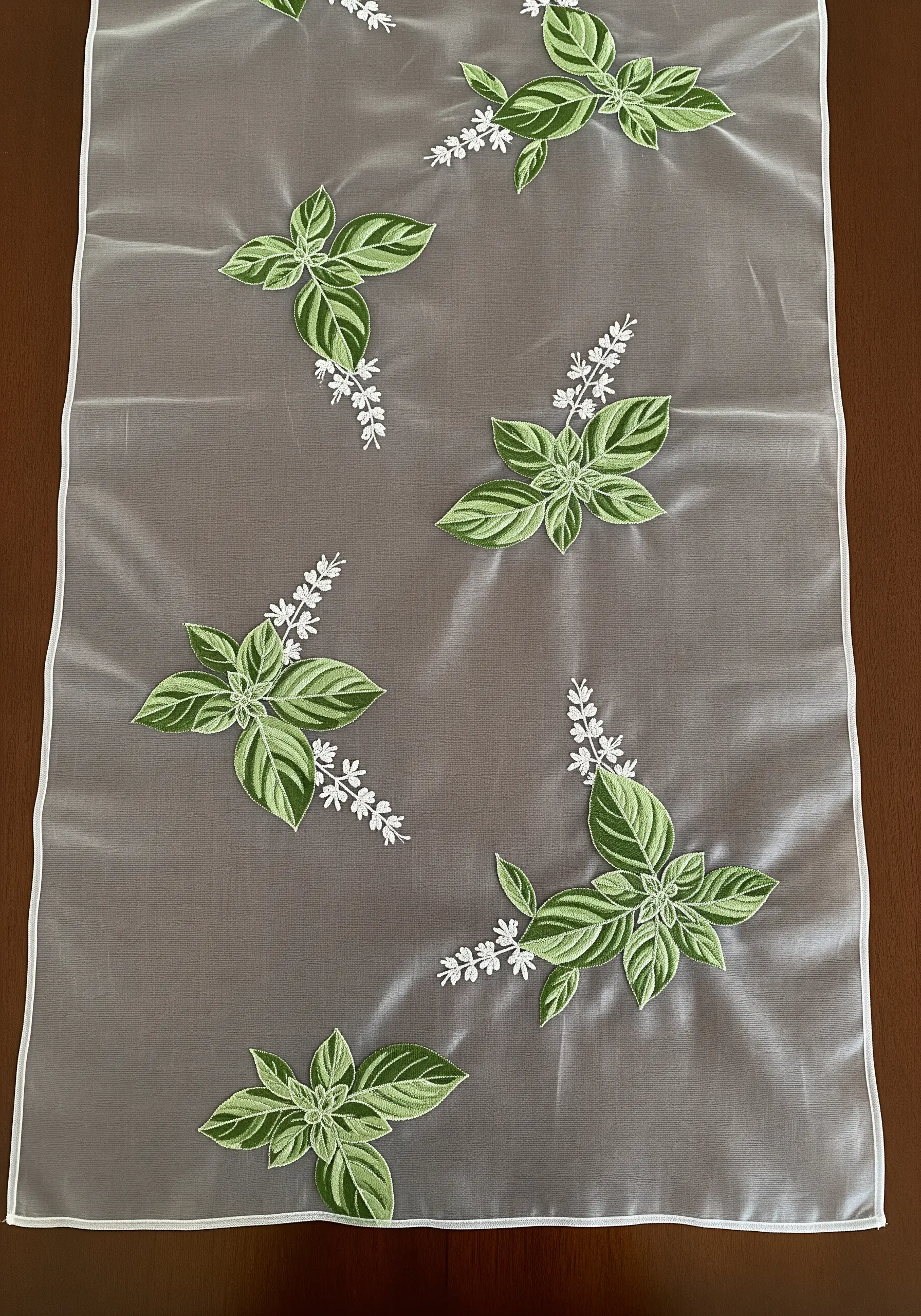 Variegated basil leaves and white blossoms embroidered on a sheer, translucent table runner.