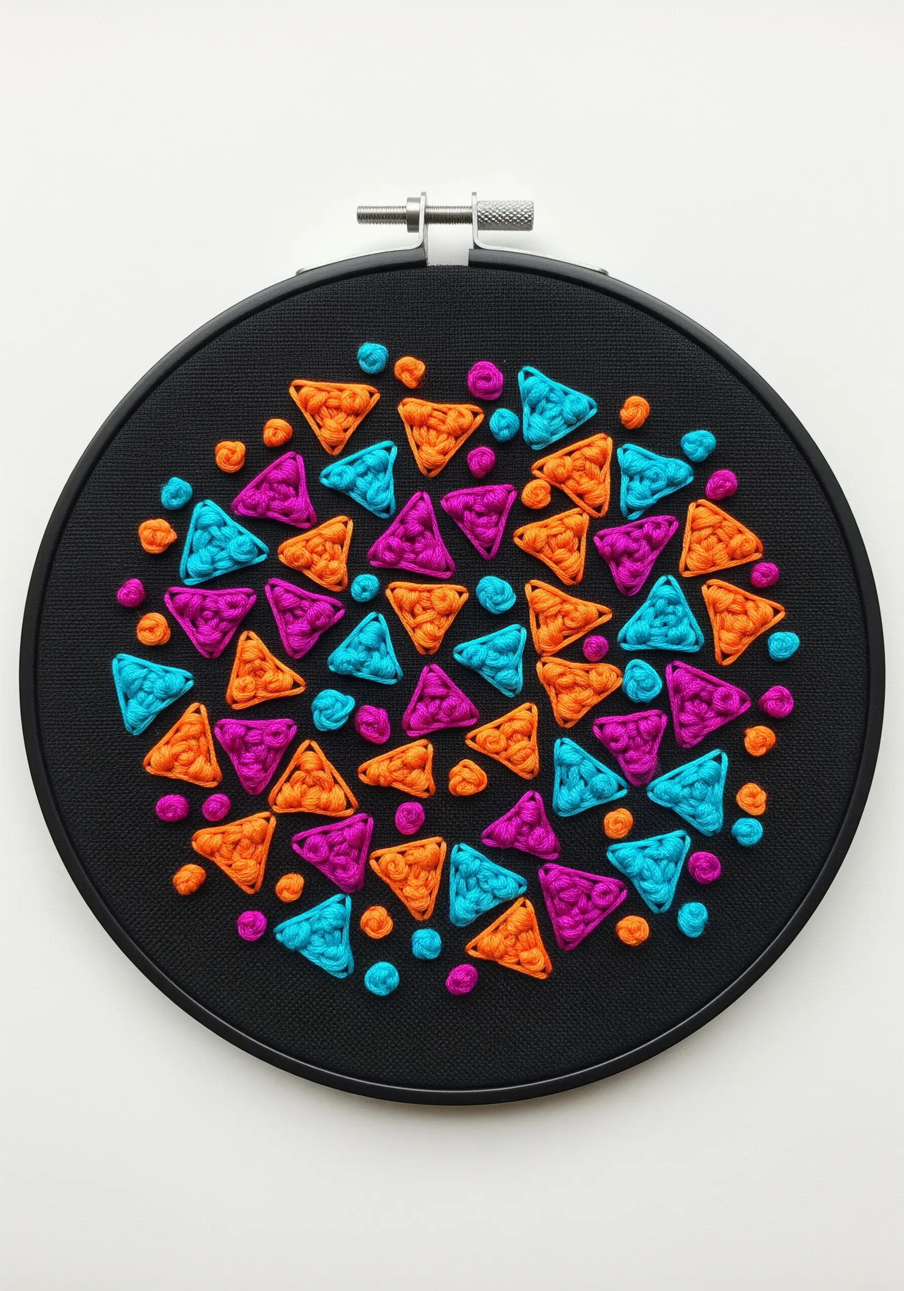 Colorful padded satin stitch triangles in turquoise, orange, and magenta on black fabric.
