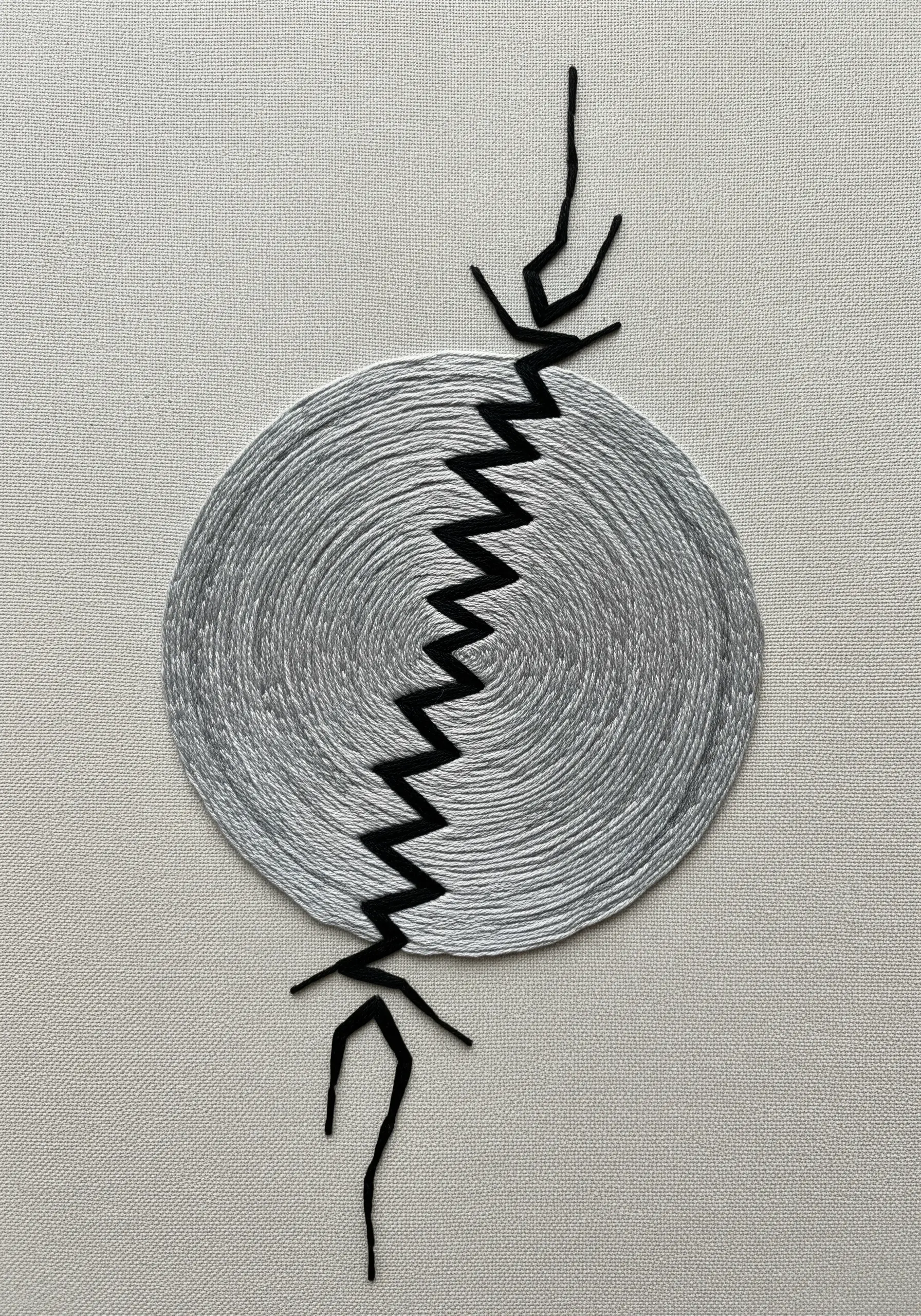 A silver stitched circle is broken in half by a sharp black zigzag line.