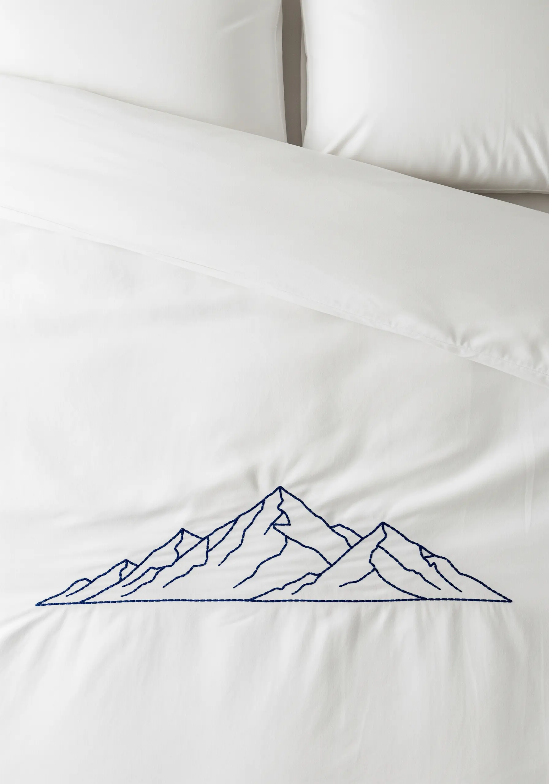 A geometric mountain range embroidered in dark blue thread on a white duvet cover.