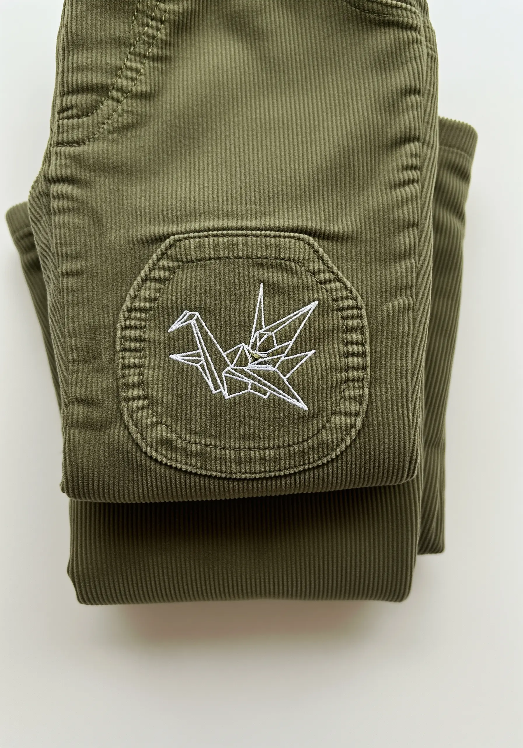 White thread origami crane embroidered on an olive green corduroy knee patch.