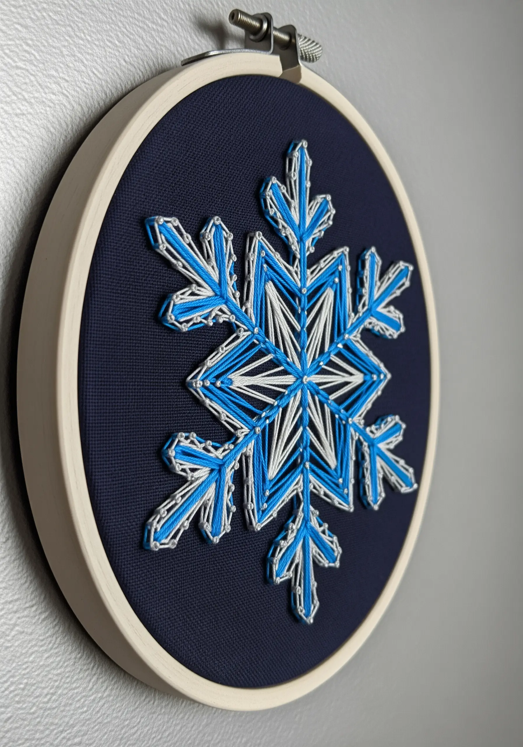 A geometric snowflake embroidered with layered white and blue outlines on dark blue fabric.