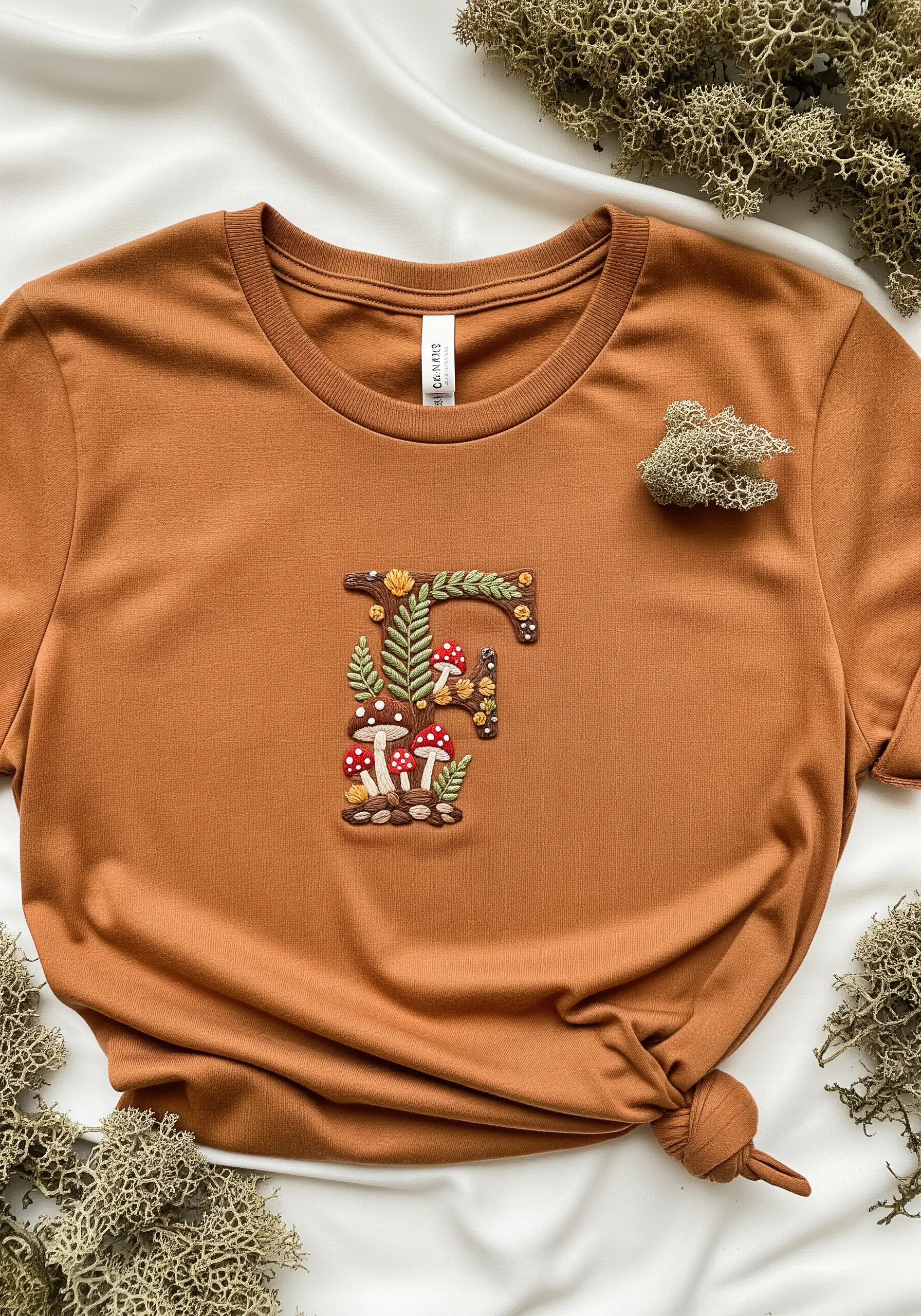 A letter 'F' filled with intricately embroidered mushrooms, ferns, and other woodland elements.